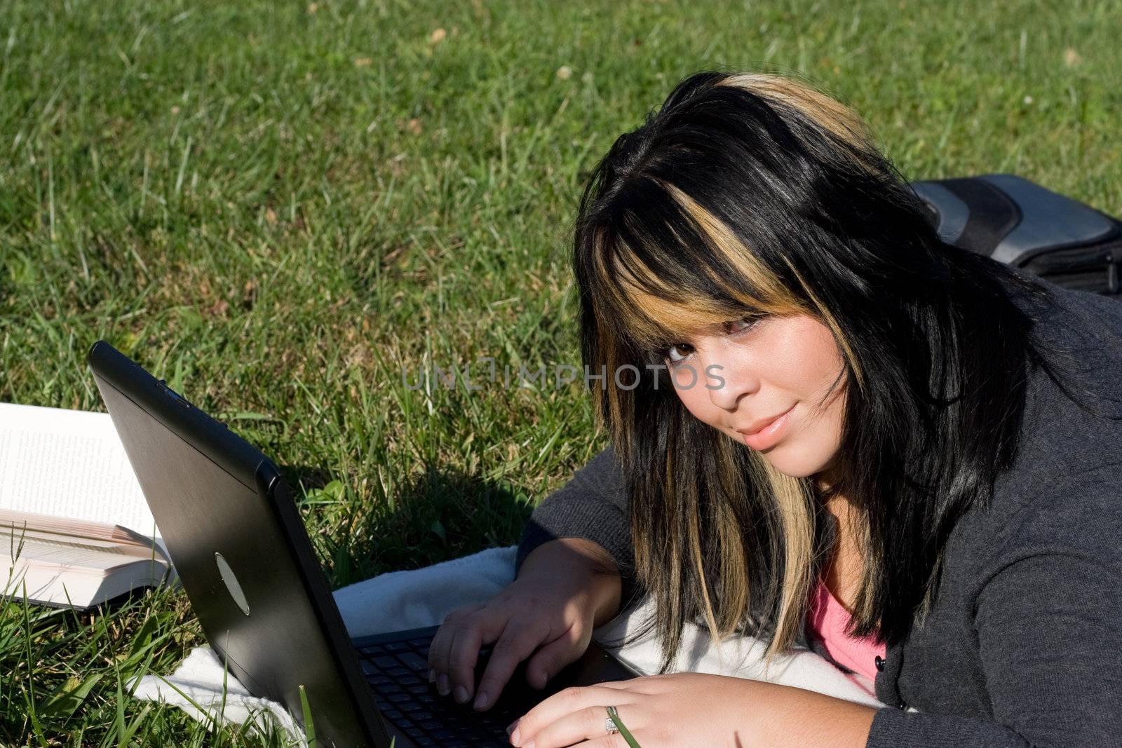 A young student using her laptop computer while laying in the grass on a nice day.