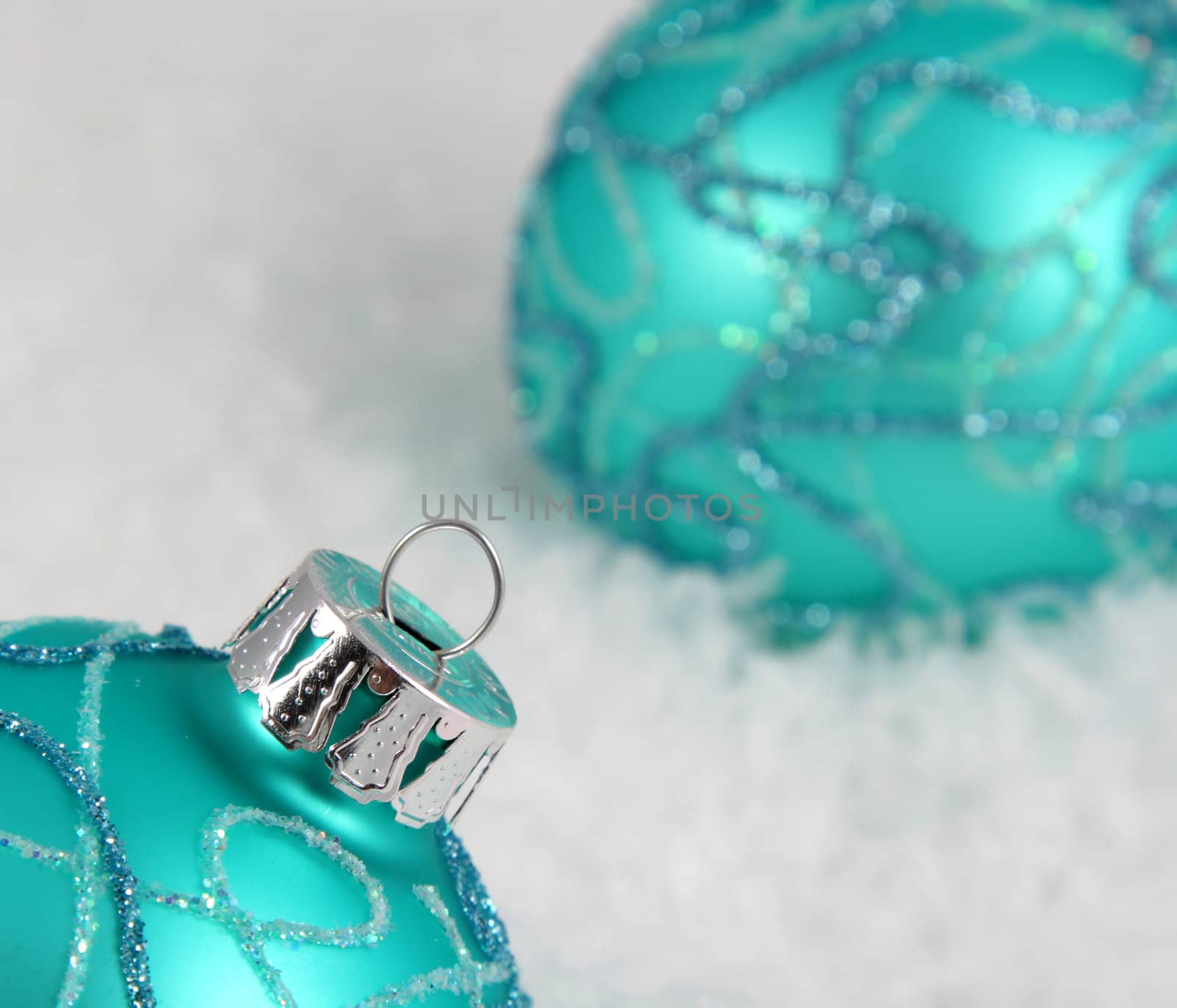 Two aqua Christmas baubles sitting in the snow.