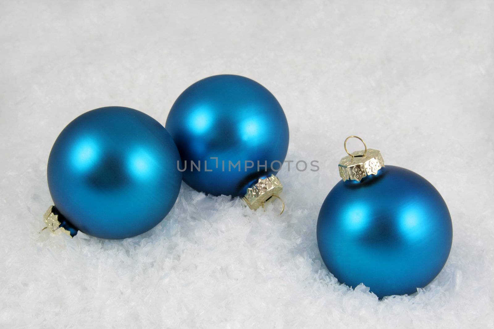 Three blue Christmas baubles sitting in snow.