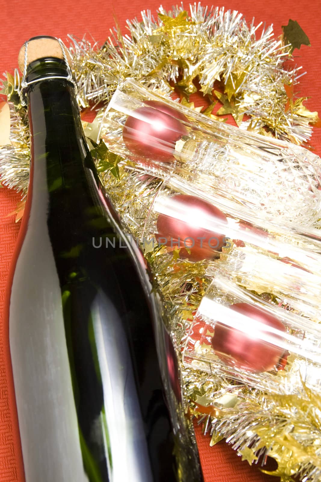 Three glasses with wine bottle and Christmas decoration on red background.