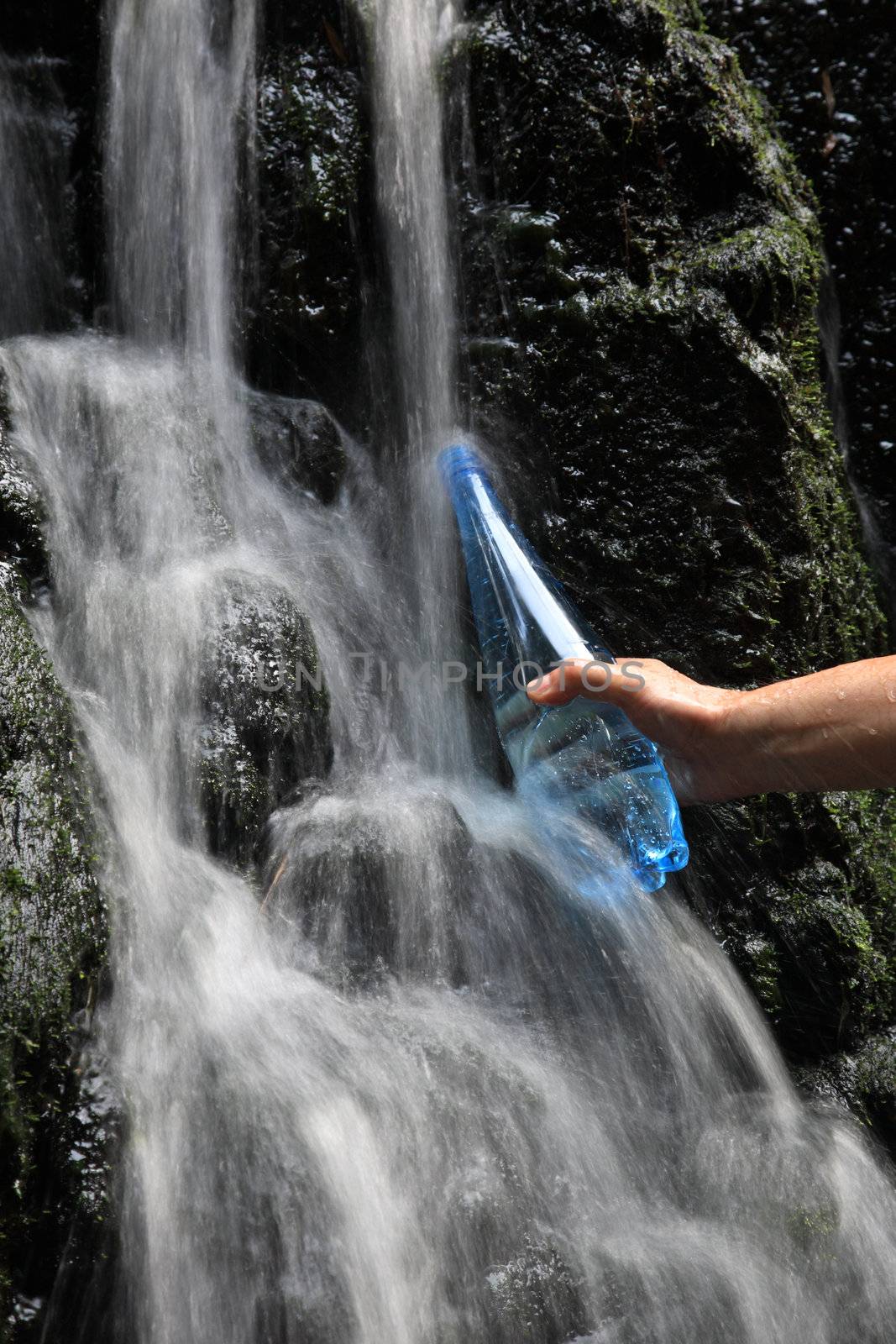 A man's hand fills a bottle of mineral water in waterfalls