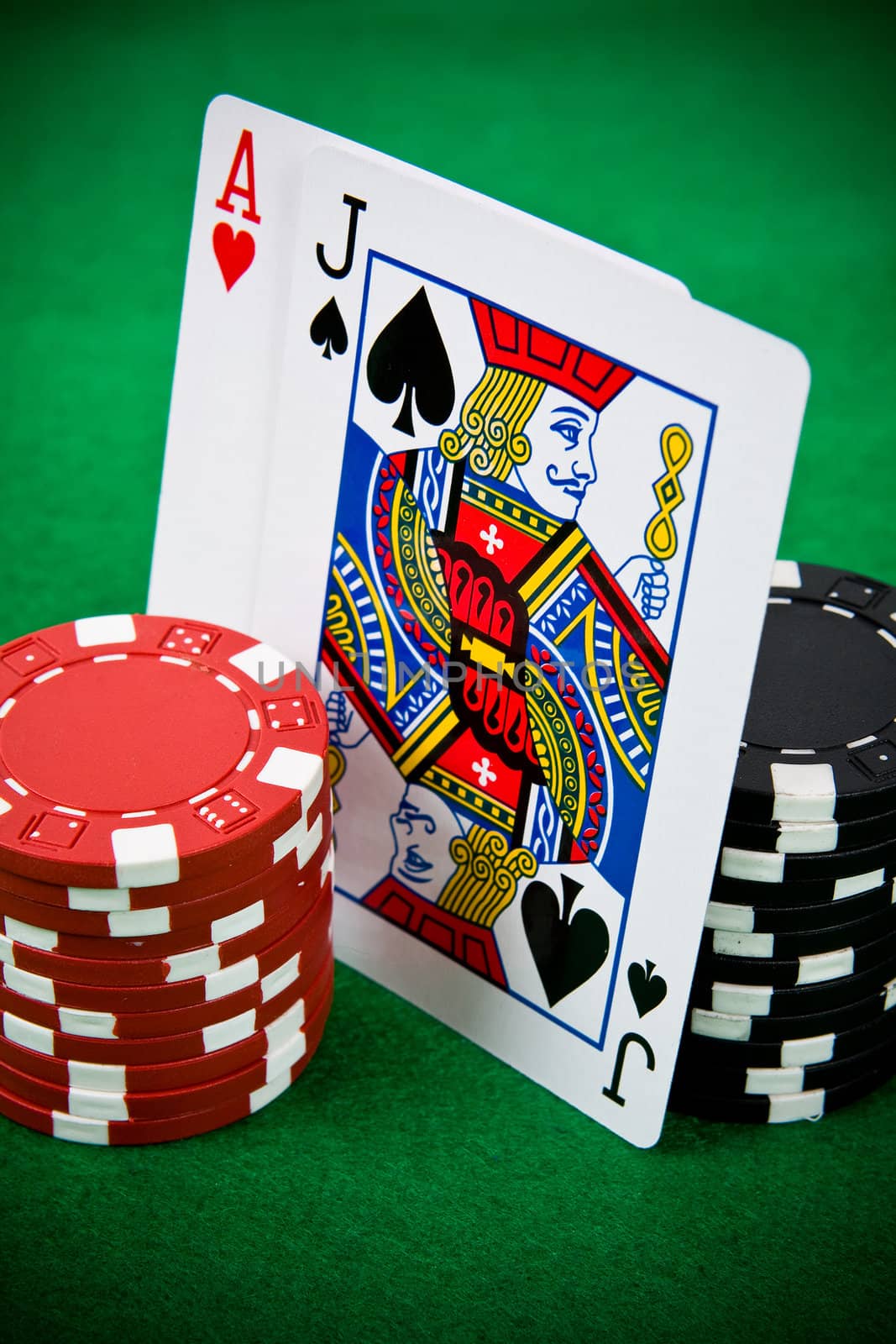 Ace of hearts and black jack with black and red poker chips on green poker table.