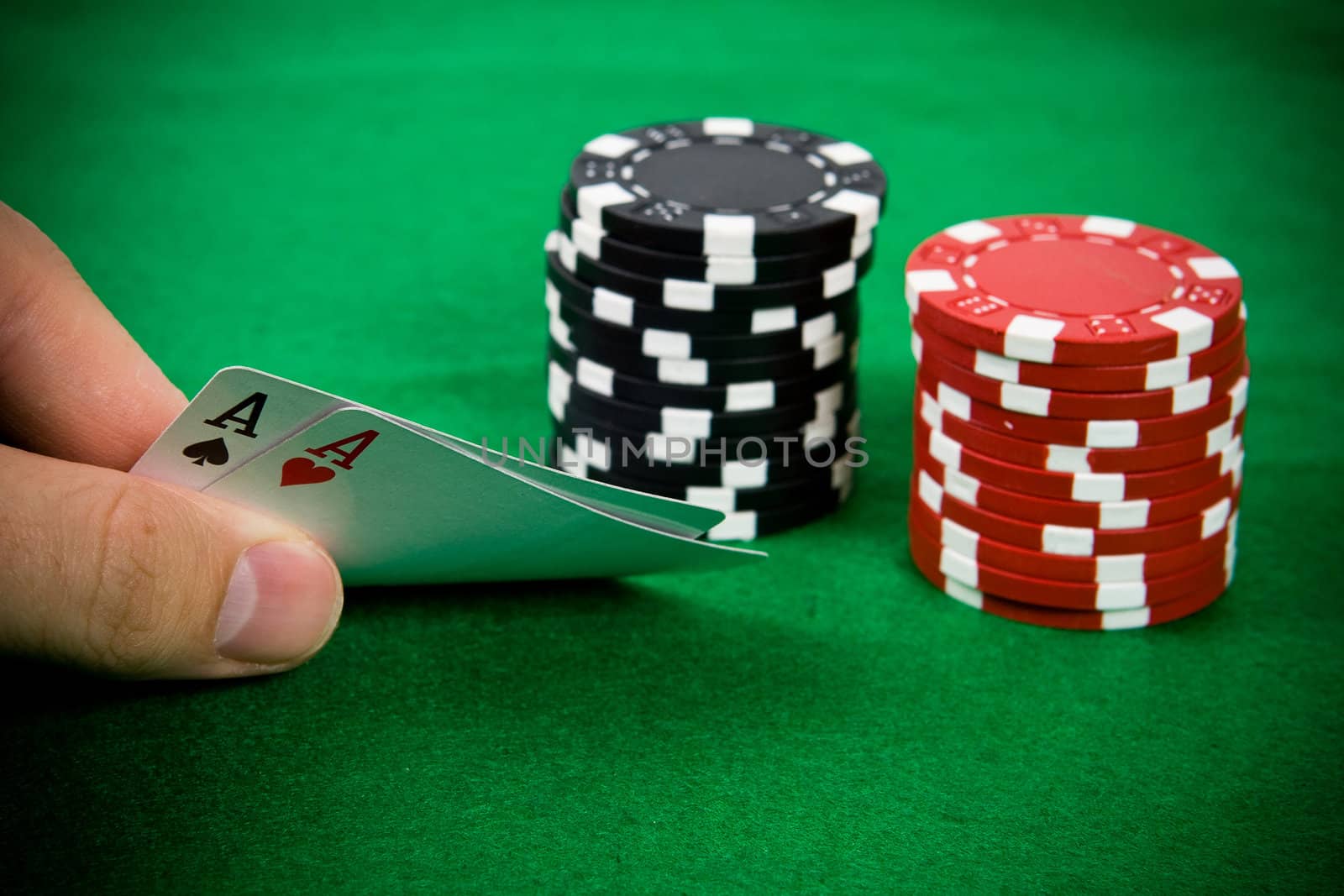 Two aces in male hand with black and red poker chips in the background.