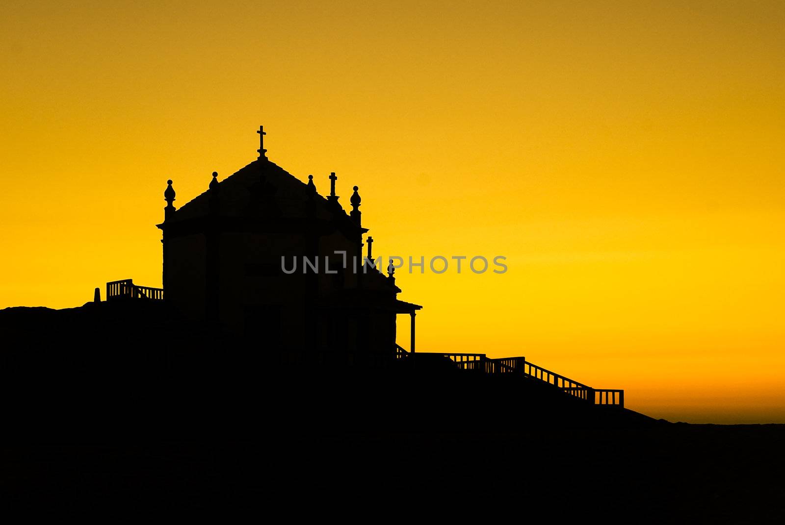 A silhouette of a chapel near the sea with a sunset sky on the background.