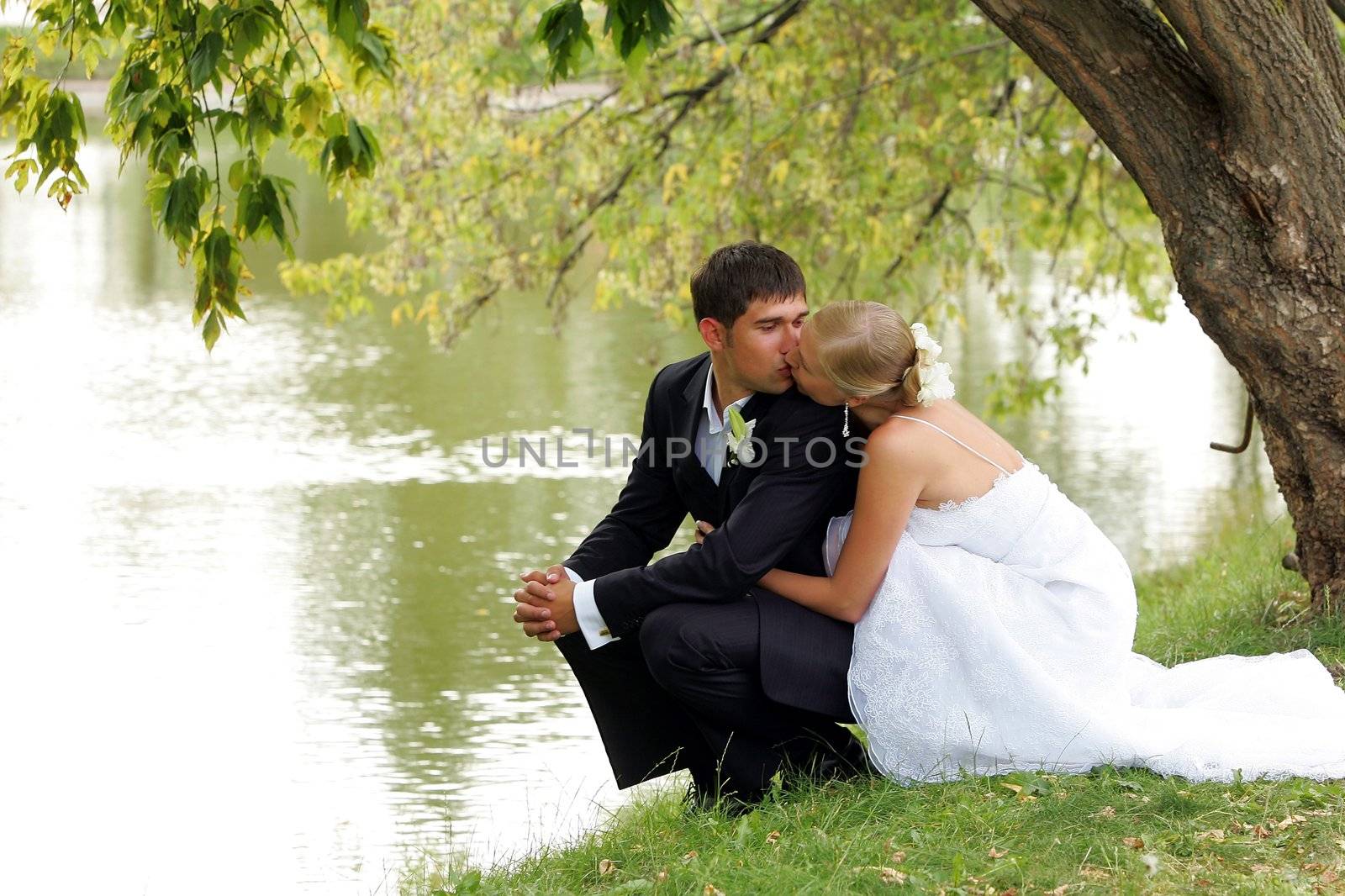 Newlywed couple kissingby lake in romantic scene.
