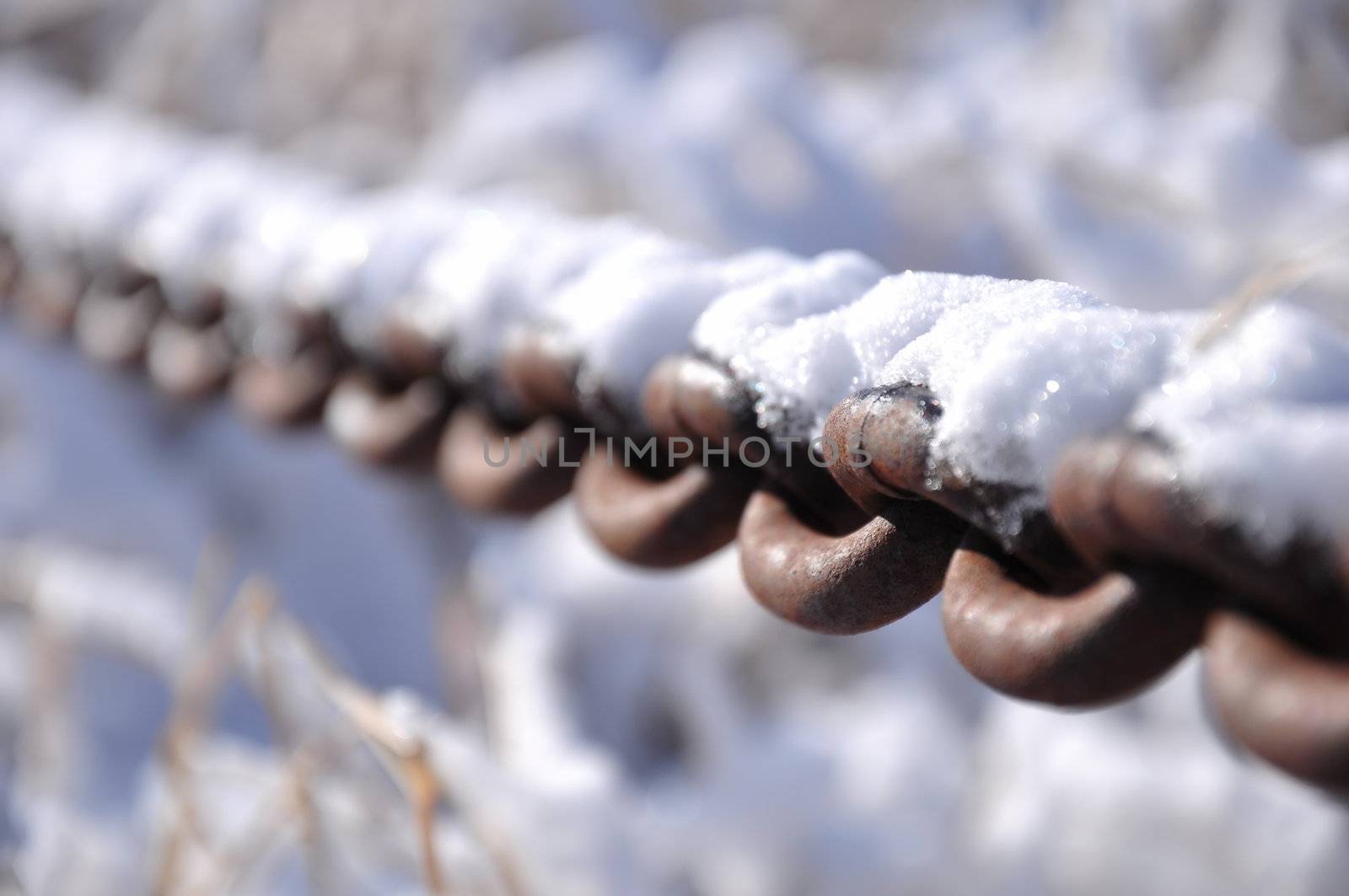 A rusty old chain covered in fresh snow on a sunny wintry day.