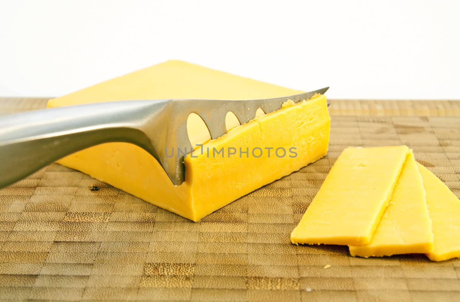 Sliced Yellow cheese with a knife on a wooden chopping board