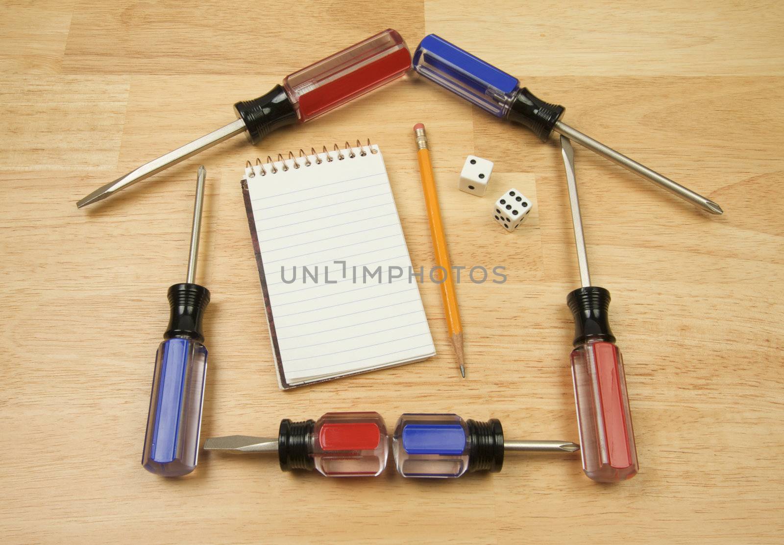House Shaped by Screwdrivers and Pad of Paper with Dice on a Wood Background.