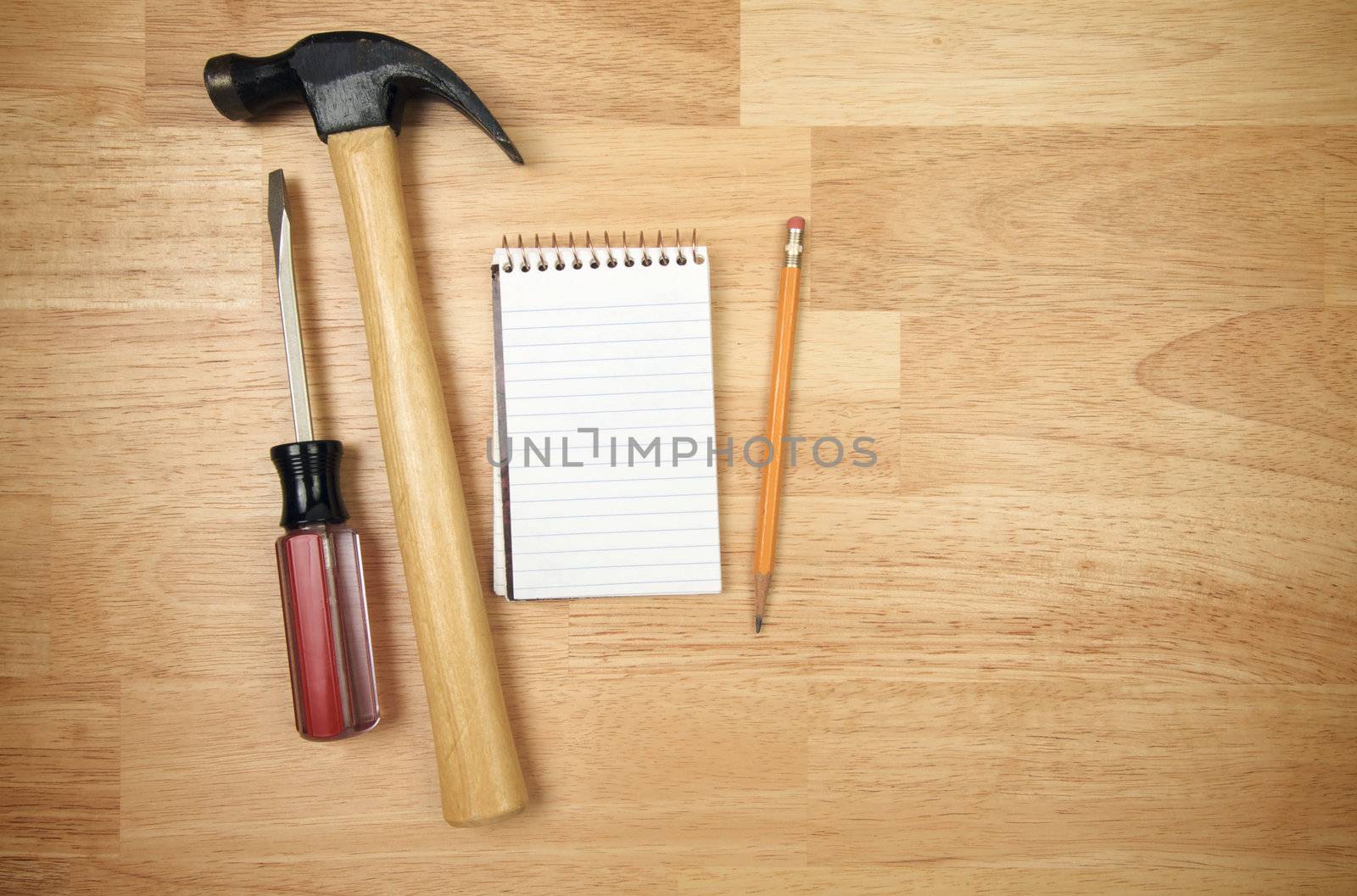 Pad of Paper, Pencil, Hammer and Screwdriver on a Wood Background.