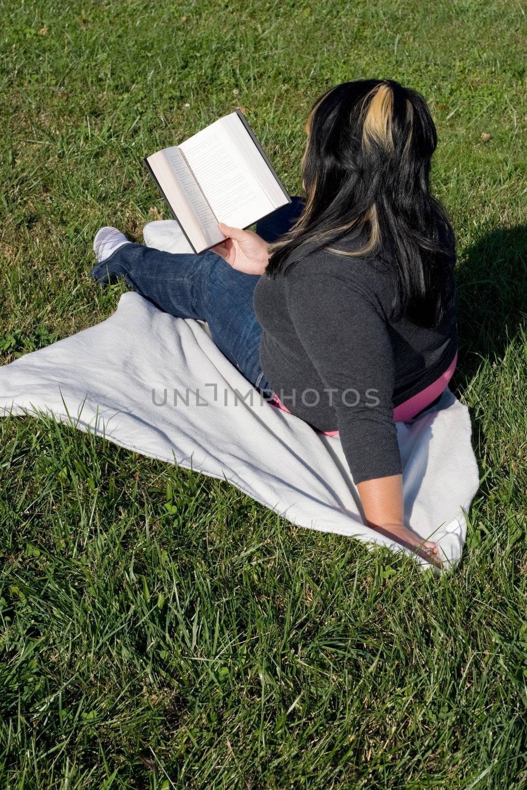 A young woman with highlighted hair reading a book on the school campus.
