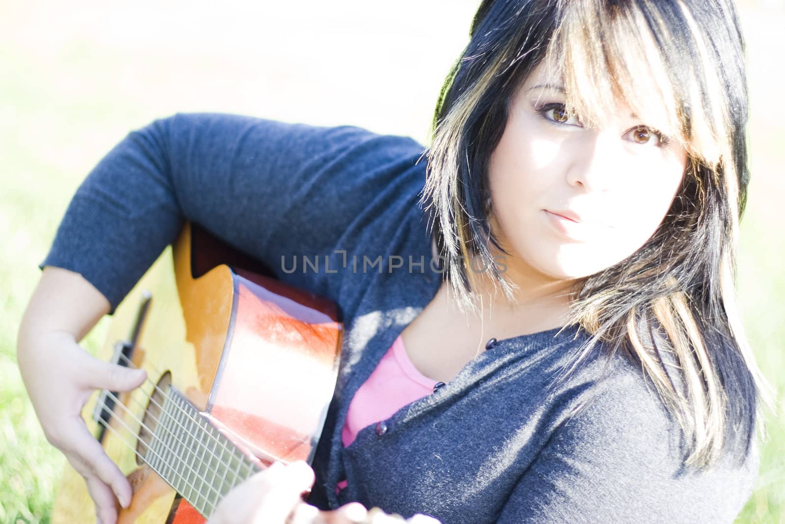 A young hispanic woman playing a guitar outdoors.