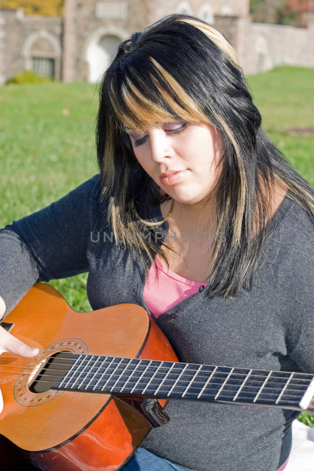 A young hispanic woman playing a guitar outdoors.