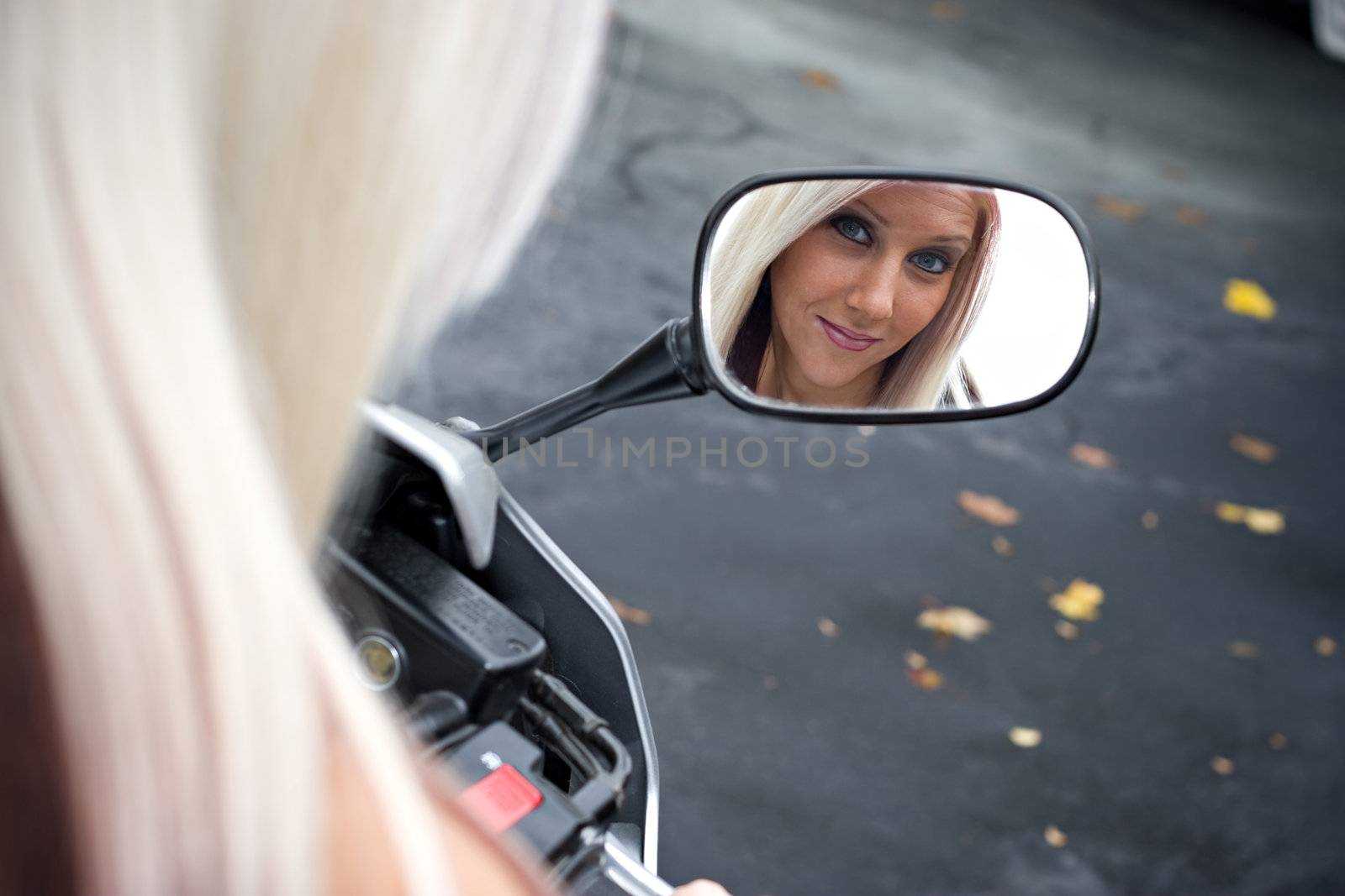 A pretty blonde woman looking into the mirror on her motorcycle.