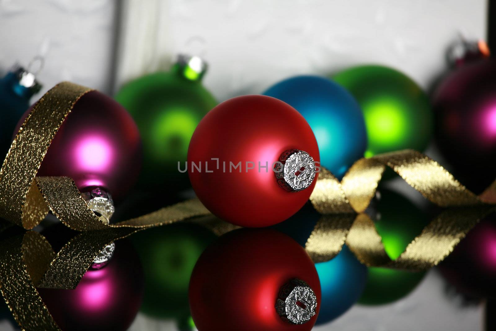 Christmas ornaments and gold ribbon on reflective surface, shallow DOF on red ornament