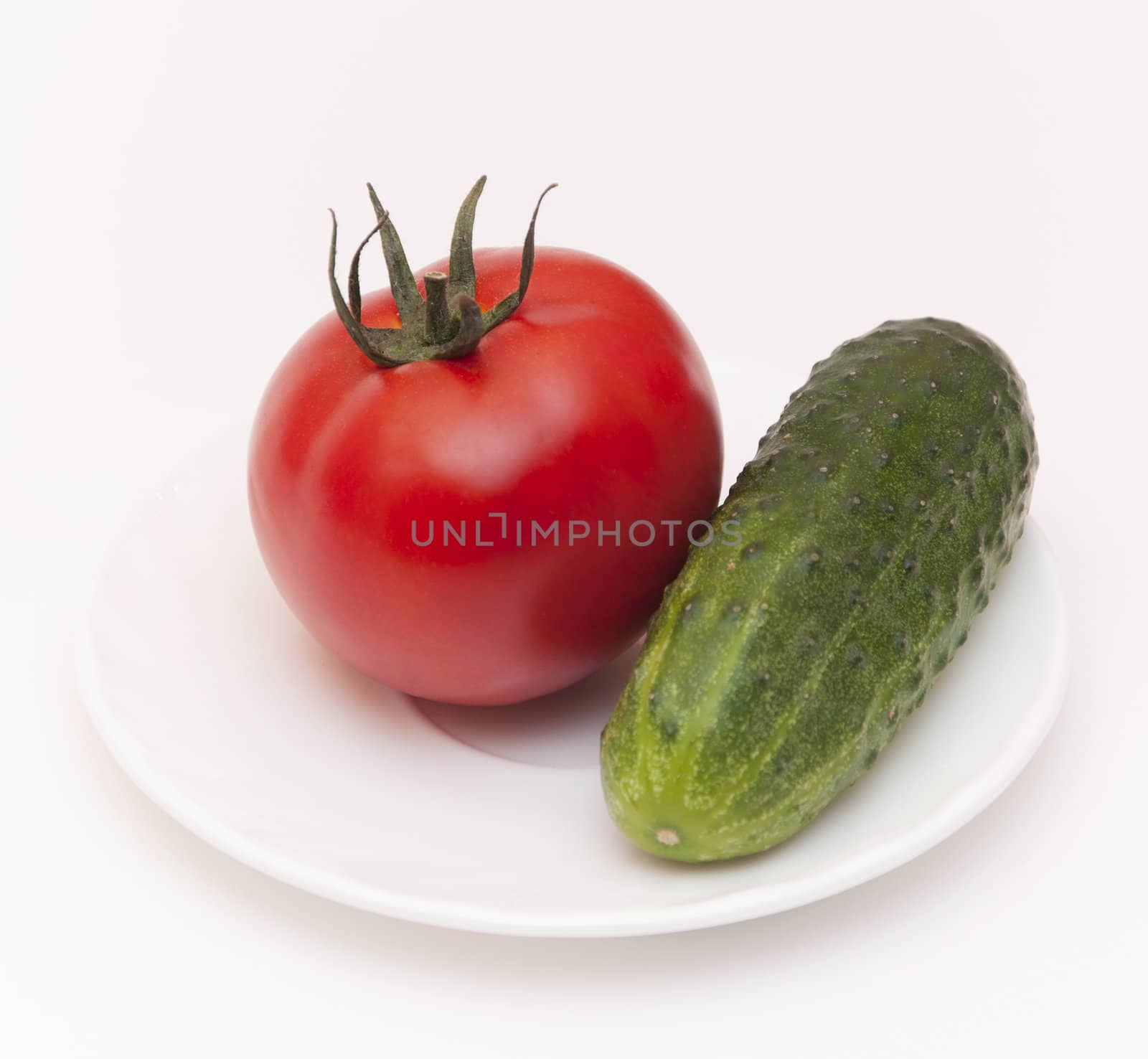 Green cucumber and red tomato on white saucer