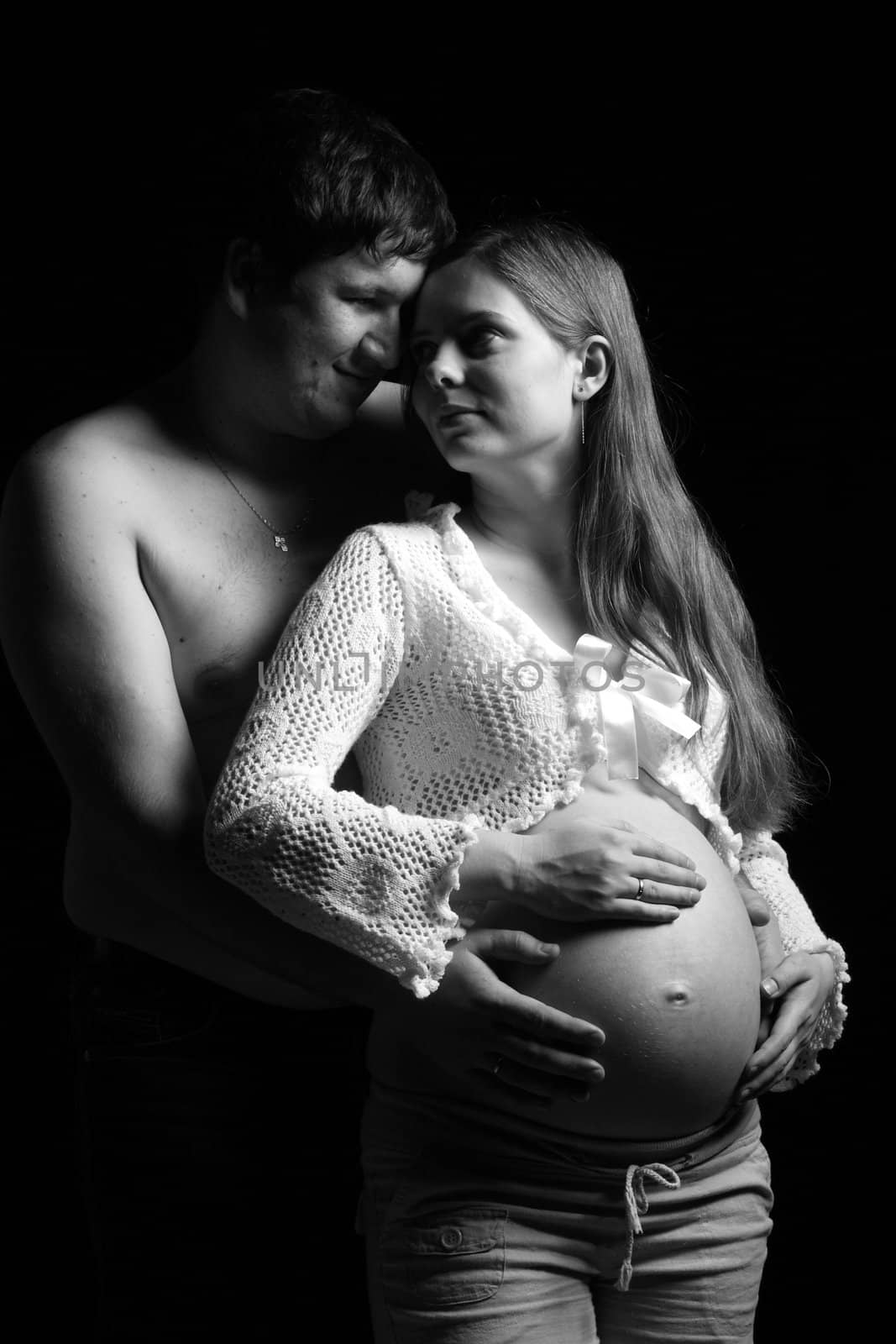 Expecting parents looking at each other and man embracing belly of his wife 