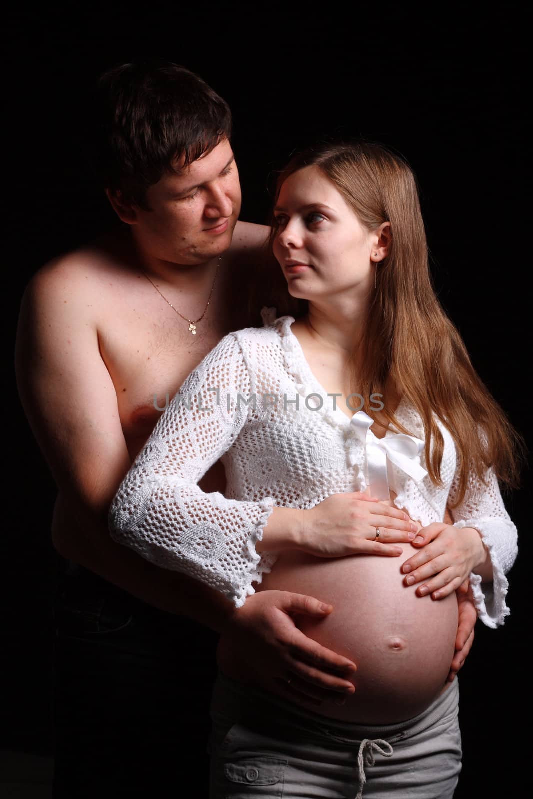 Expecting parents looking at each other and man embracing belly of his wife 
