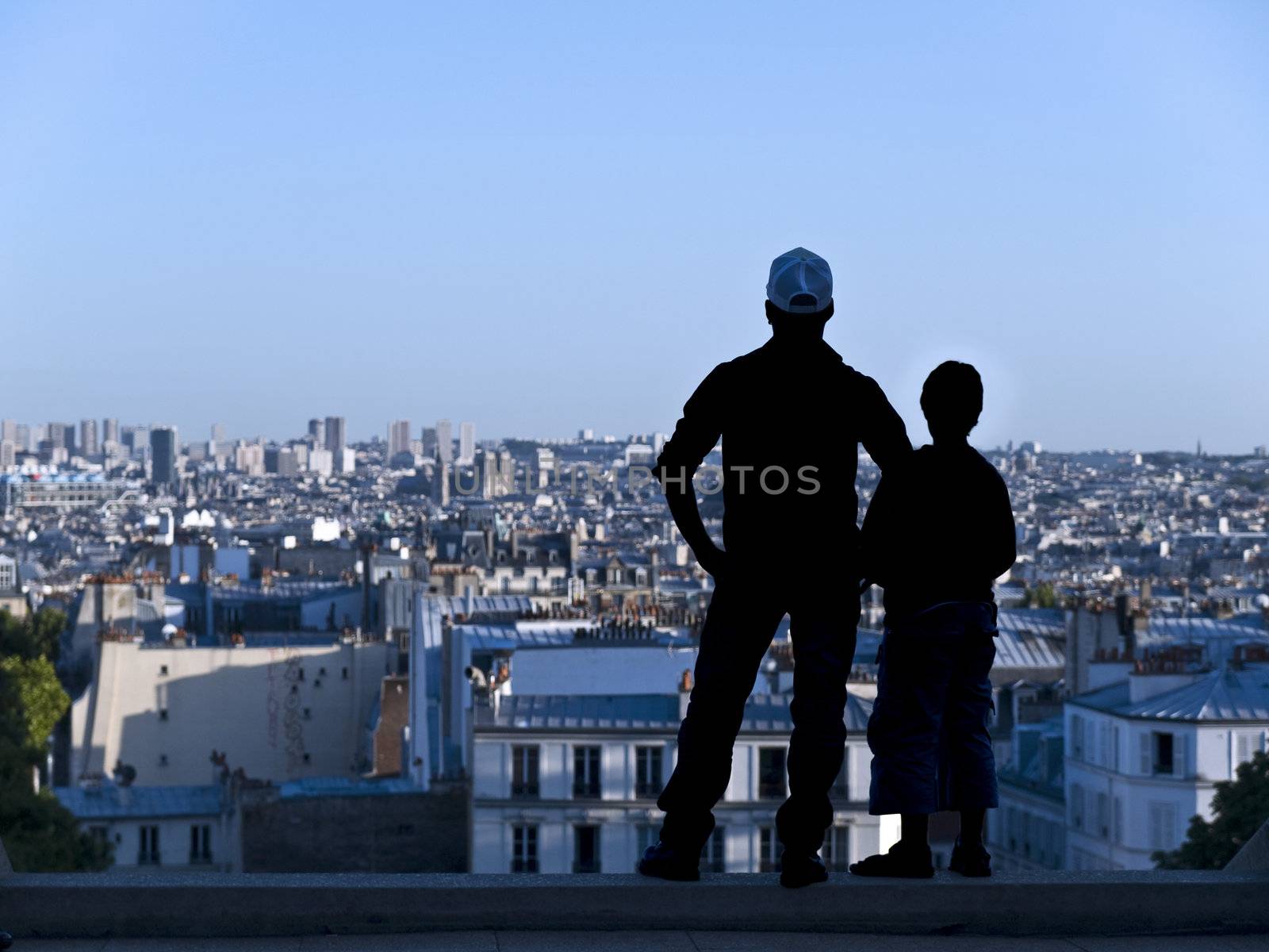 A boy and his father are looking over the roofs in Paris.