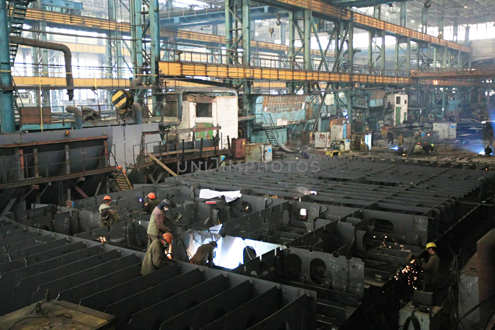 Welders welding a metal part in a dark industrial environment.