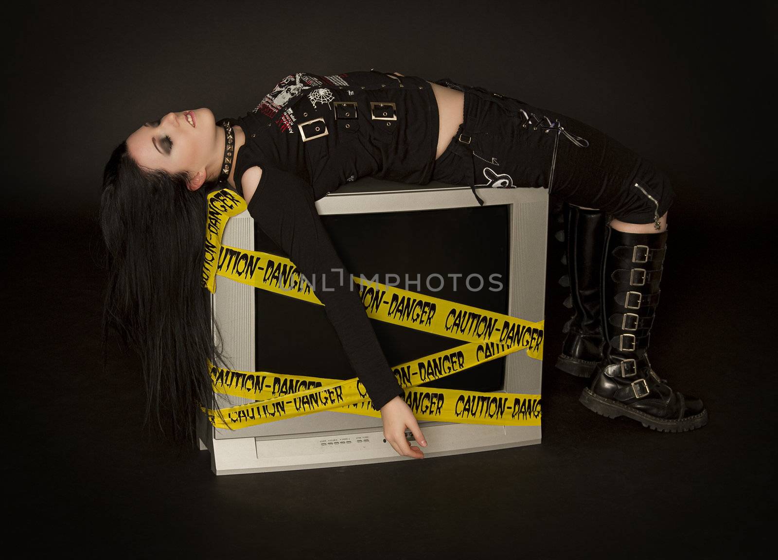 Teenage girl in goth style clothes laying on a television 