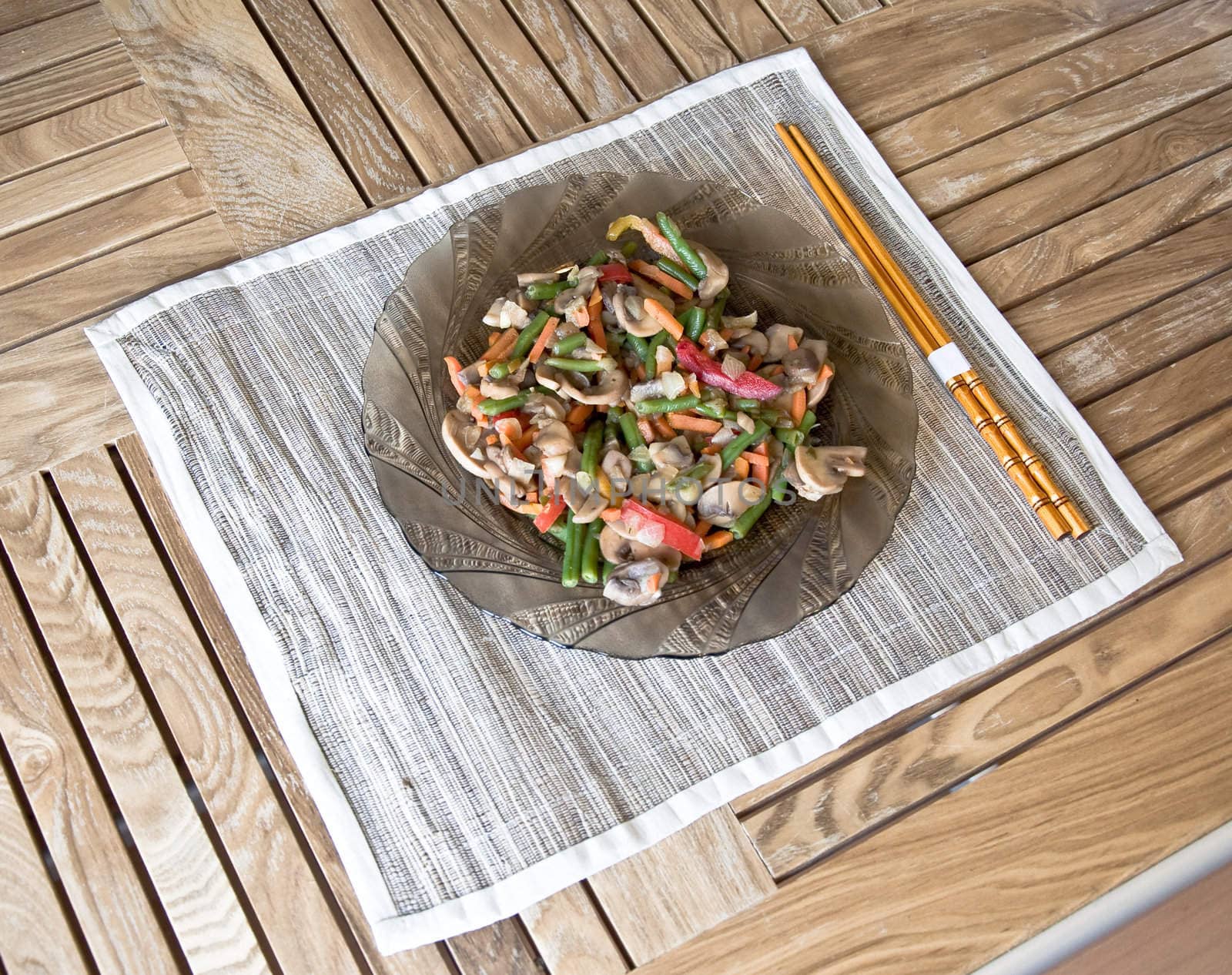 Plate with grilled vegetables and chopsticks. On wooden table.