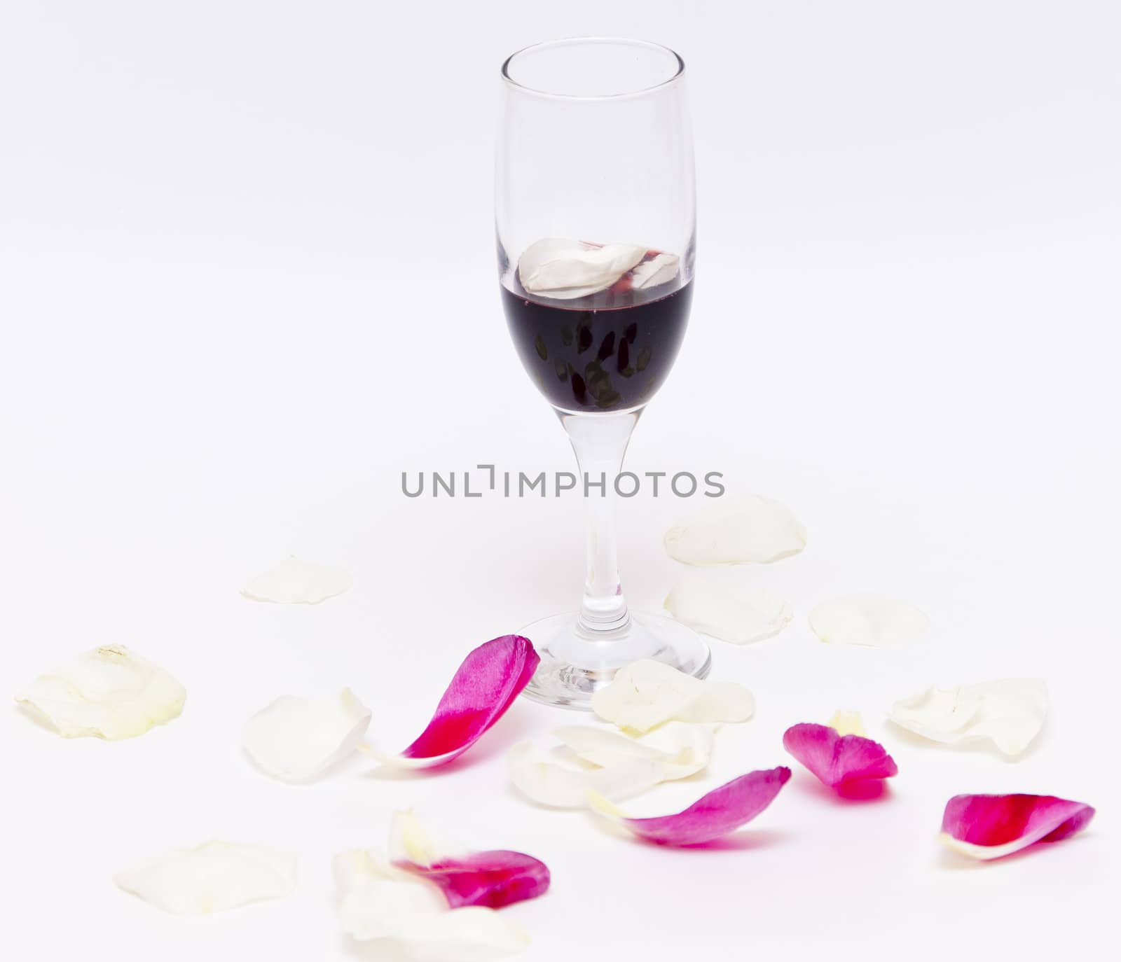 Petals of white rose with red wine glass