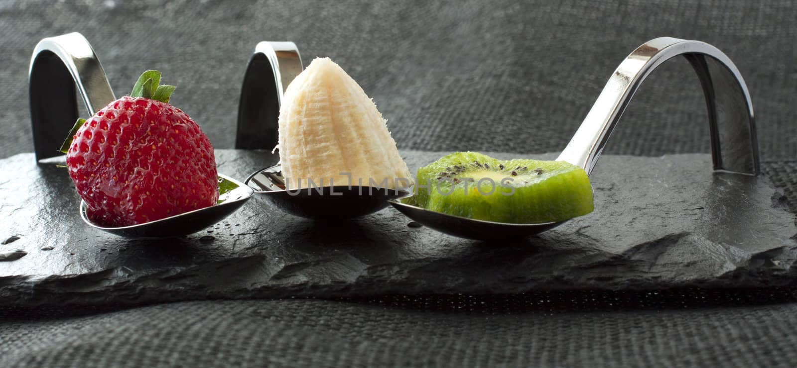 Strawberry, banana and kiwi over elegant restaurant metal spoons