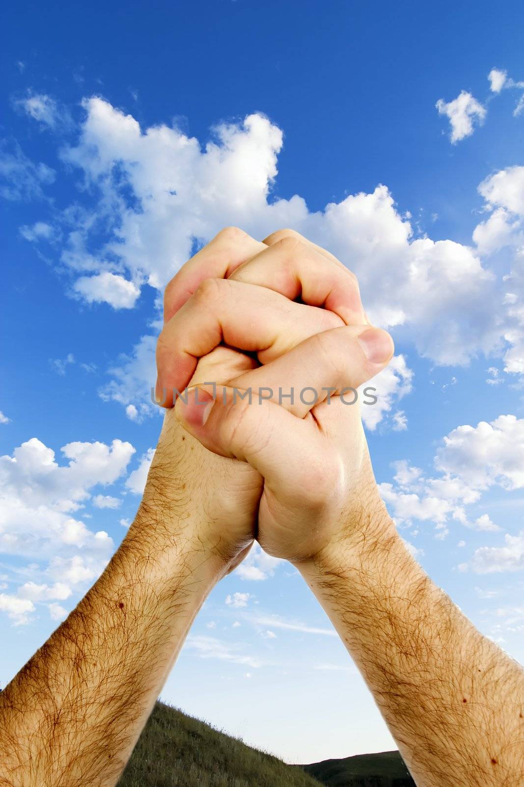 Praying hands on top of a beautiful prairie landscape with a deep blue sky and picturesque clouds.
