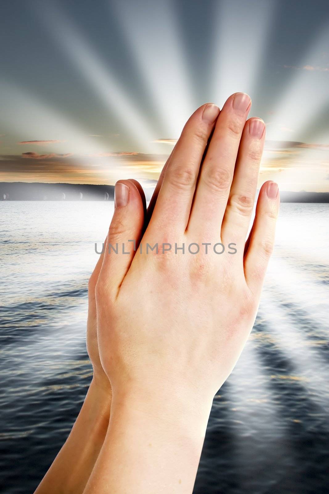 Praying hands with a landscape with the ocean and a sunset in the background