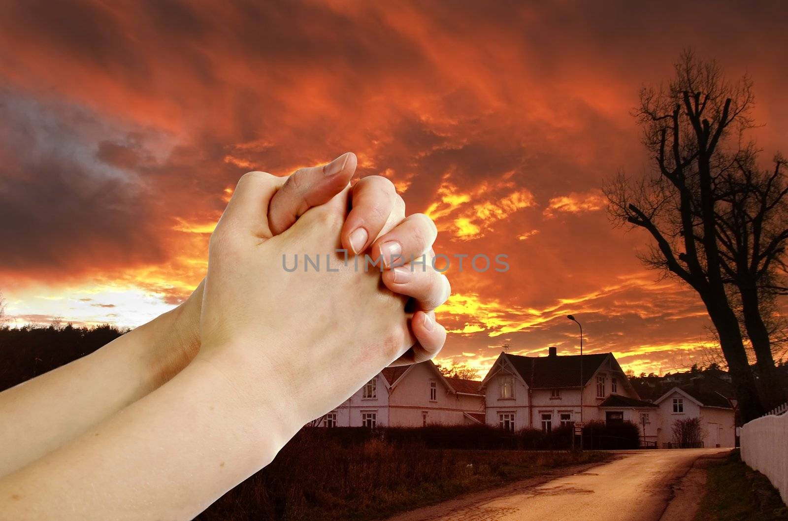 Hands praying with a dramatic red sky overa small town; prayer warrior.