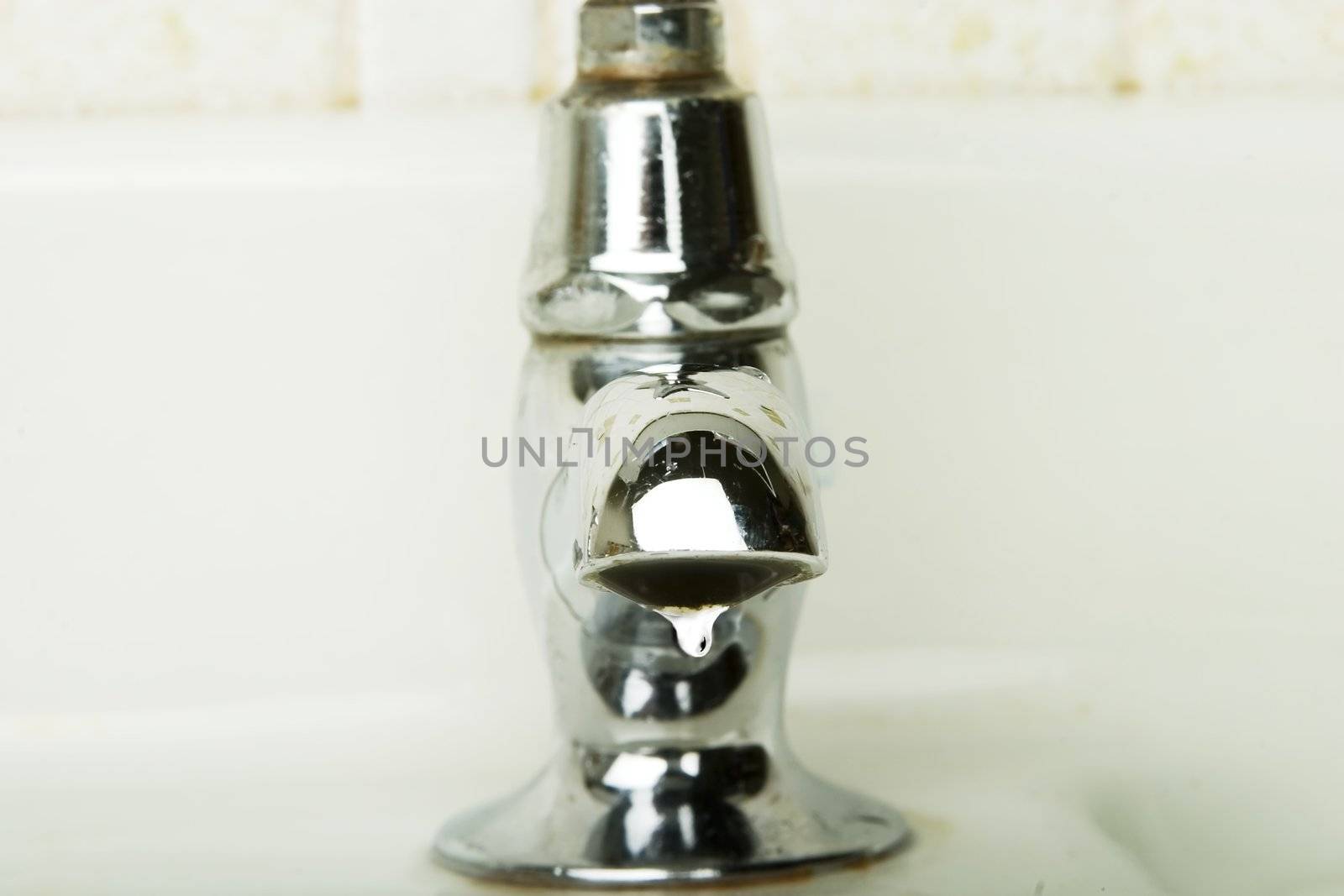 A retro sink tap and faucet.  A detail image of a water drip getting ready to drop.