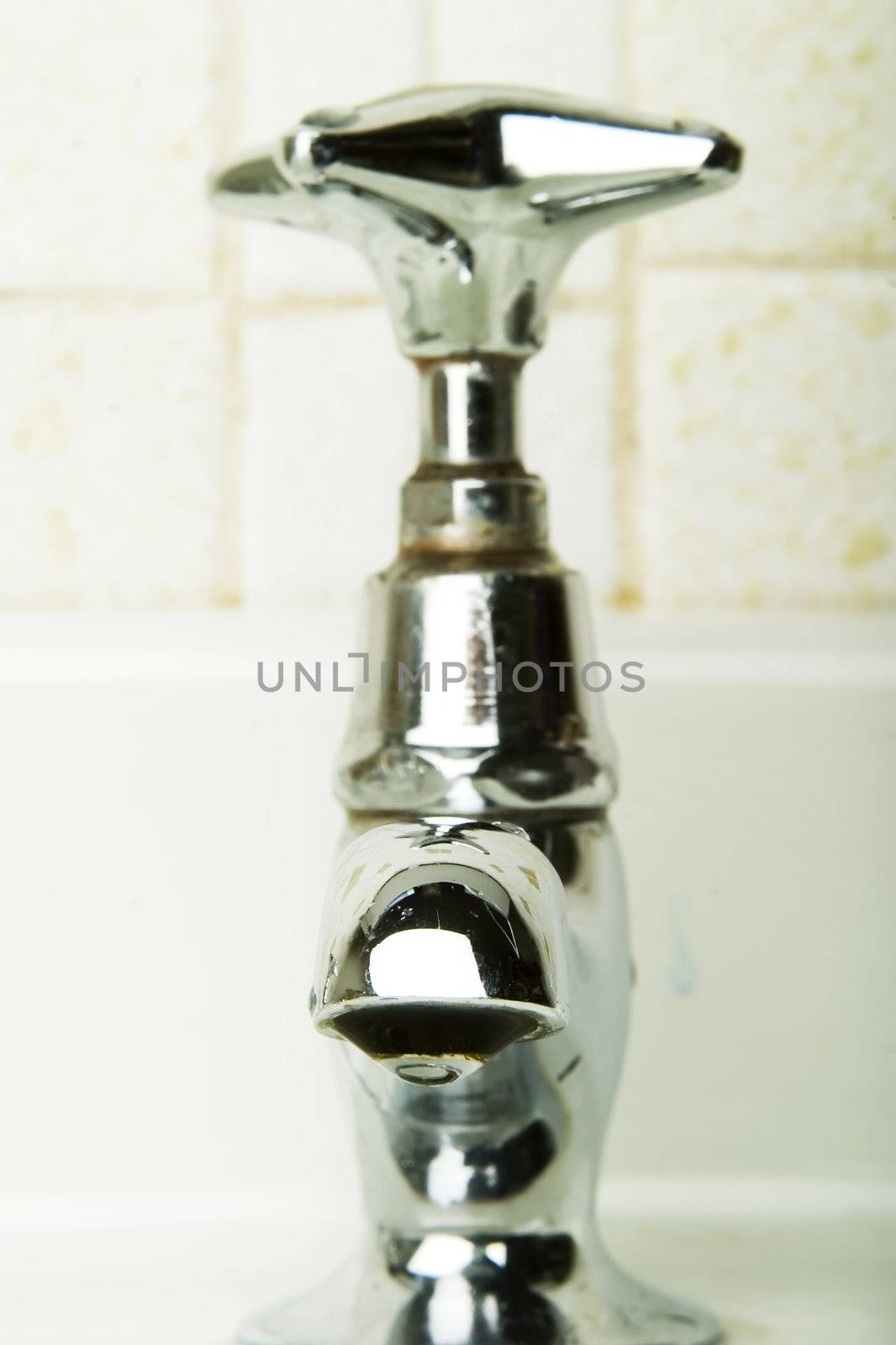 A retro sink tap and faucet with a drip gathering on the end.