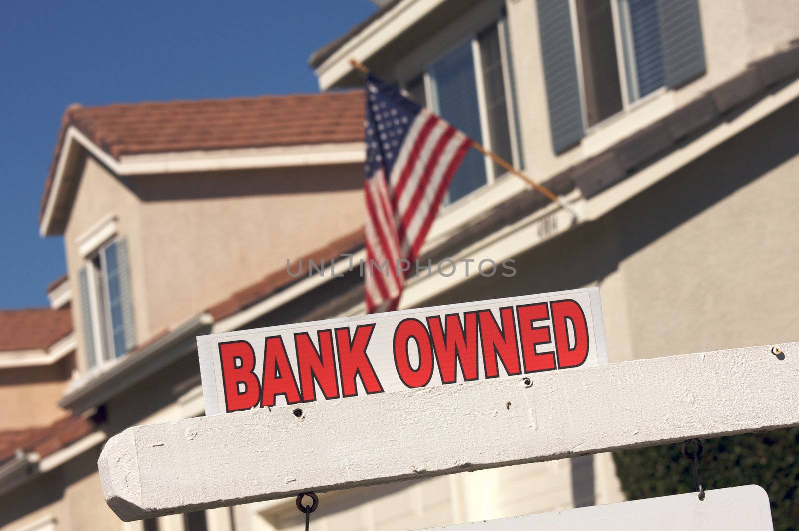 Bank Owned Real Estate Sign and House with American Flag in the Background.