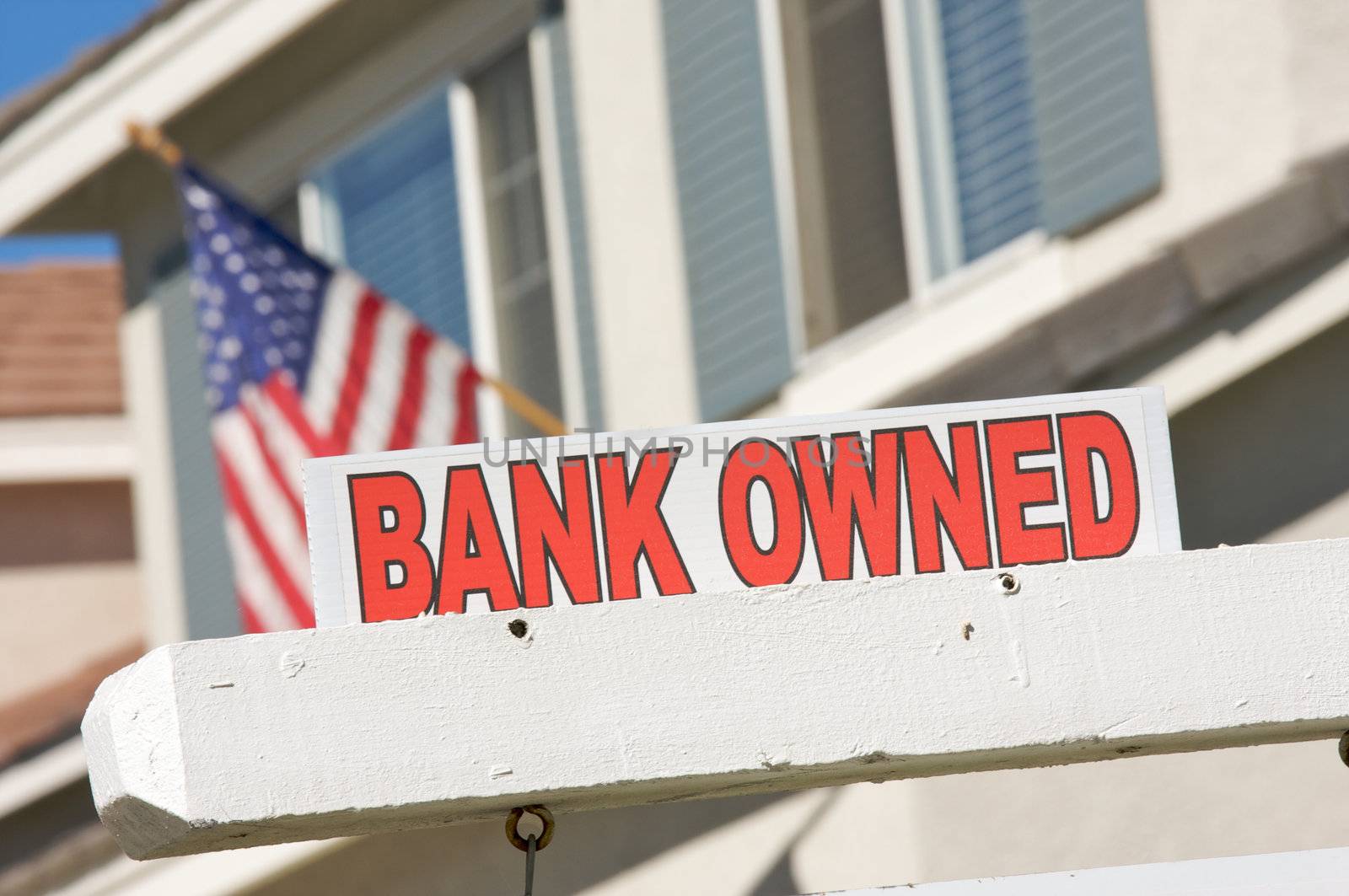 Bank Owned Real Estate Sign and House with American Flag in the Background.