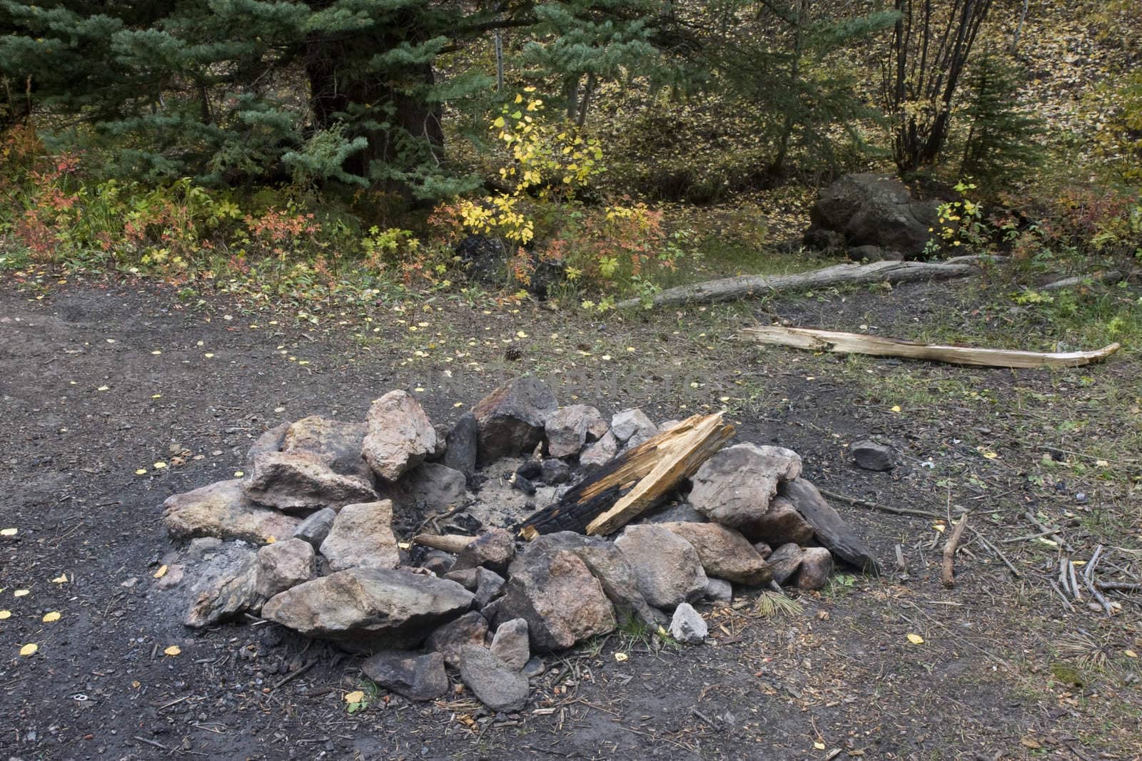 fire ring made from stones with ash and firewood in a mountain forest with fall colors