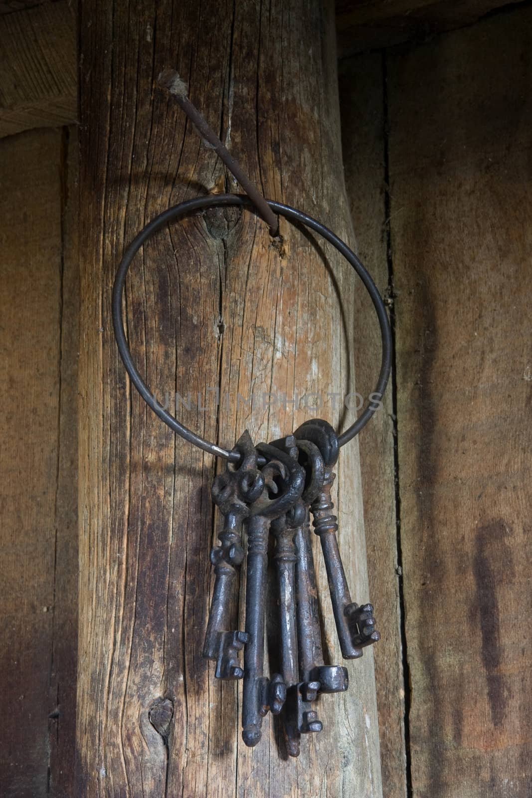 ring of five heavy vintage skeleton keys hanging on a post in a dark, rustic building