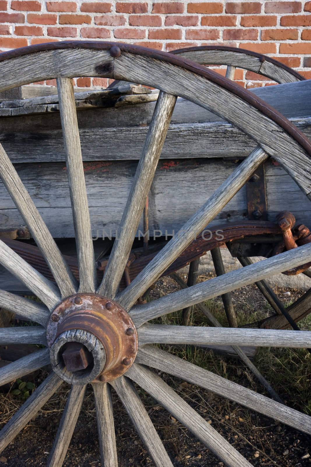 detail of an old wagon with wooden wheels againts brick wall