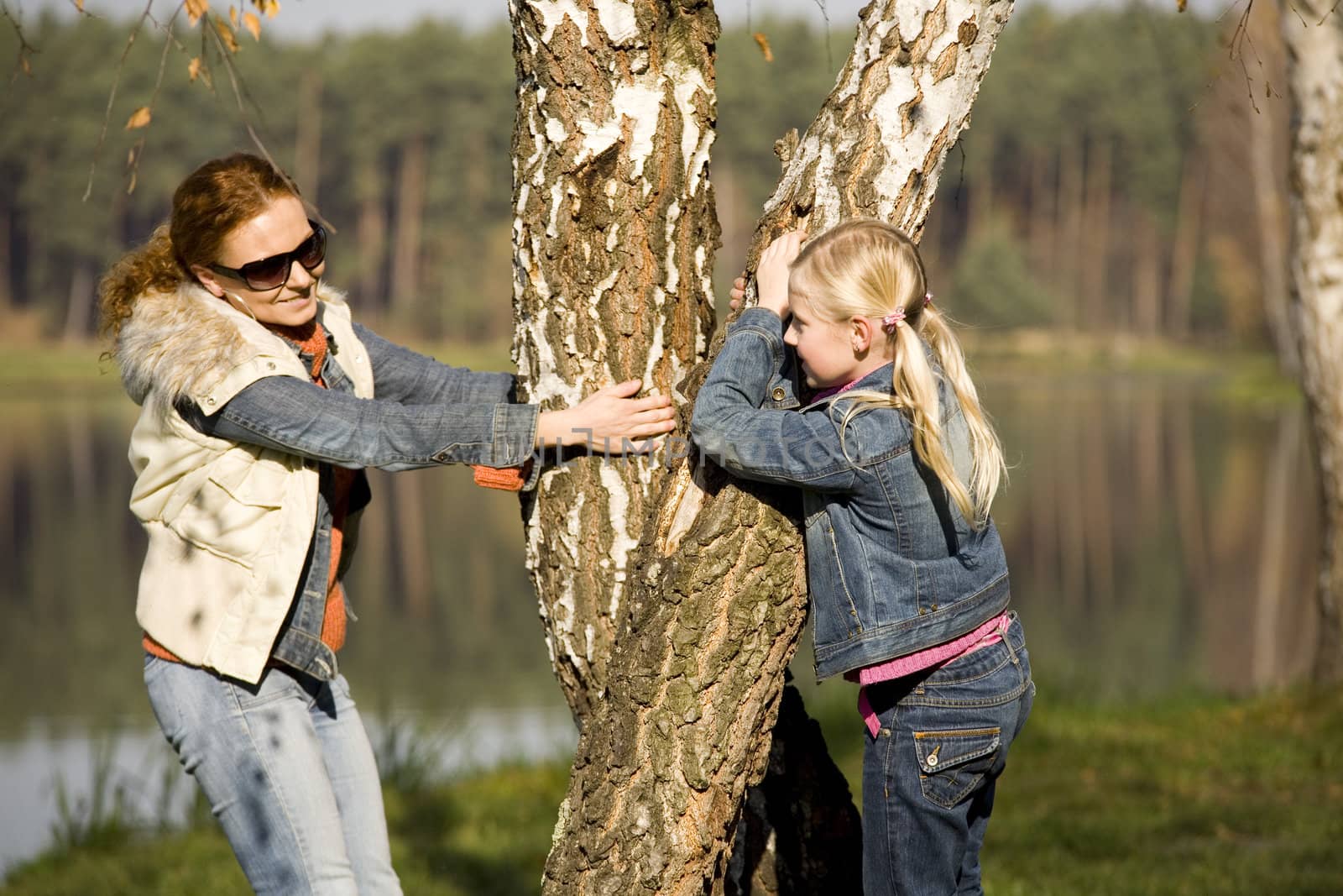 Littlt girl with mother at the lake in the forest, is a warm, sunny autumn day.