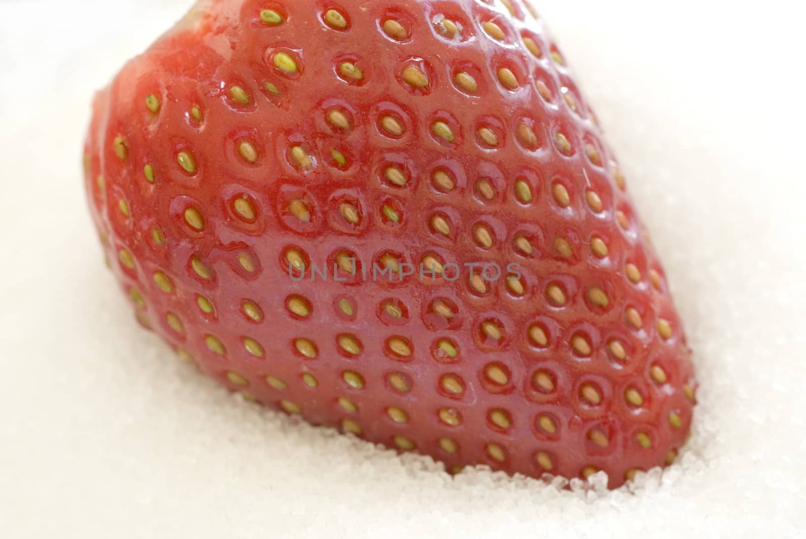 high key image of a single ripe strawberry on a bed of sugar granuals