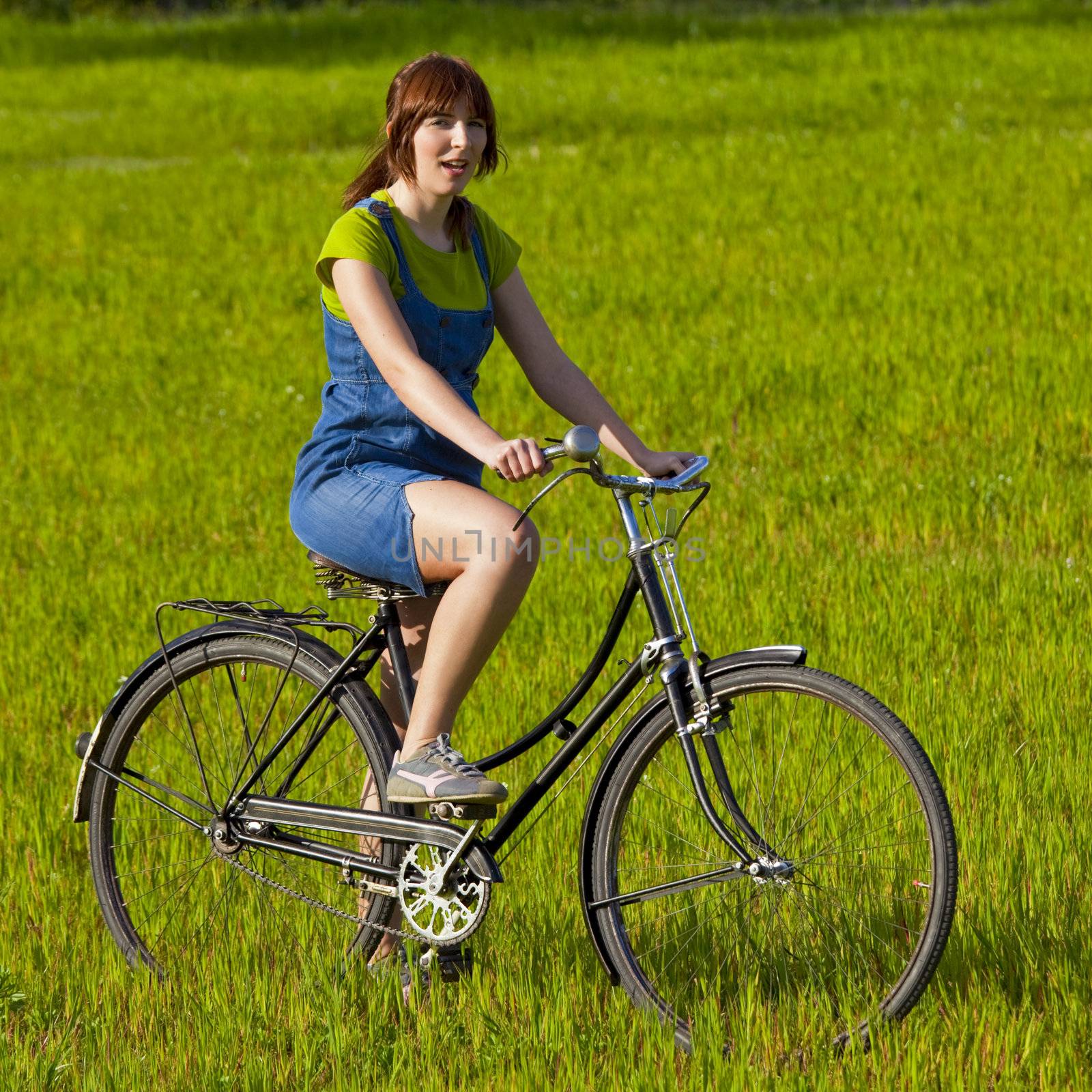 Happy young woman on a green meadow riding a bicycle