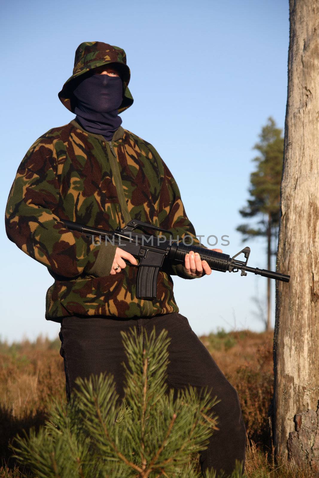 A soldier holding a M16 (AR-15) Rifle with camouflage and a balaclava.