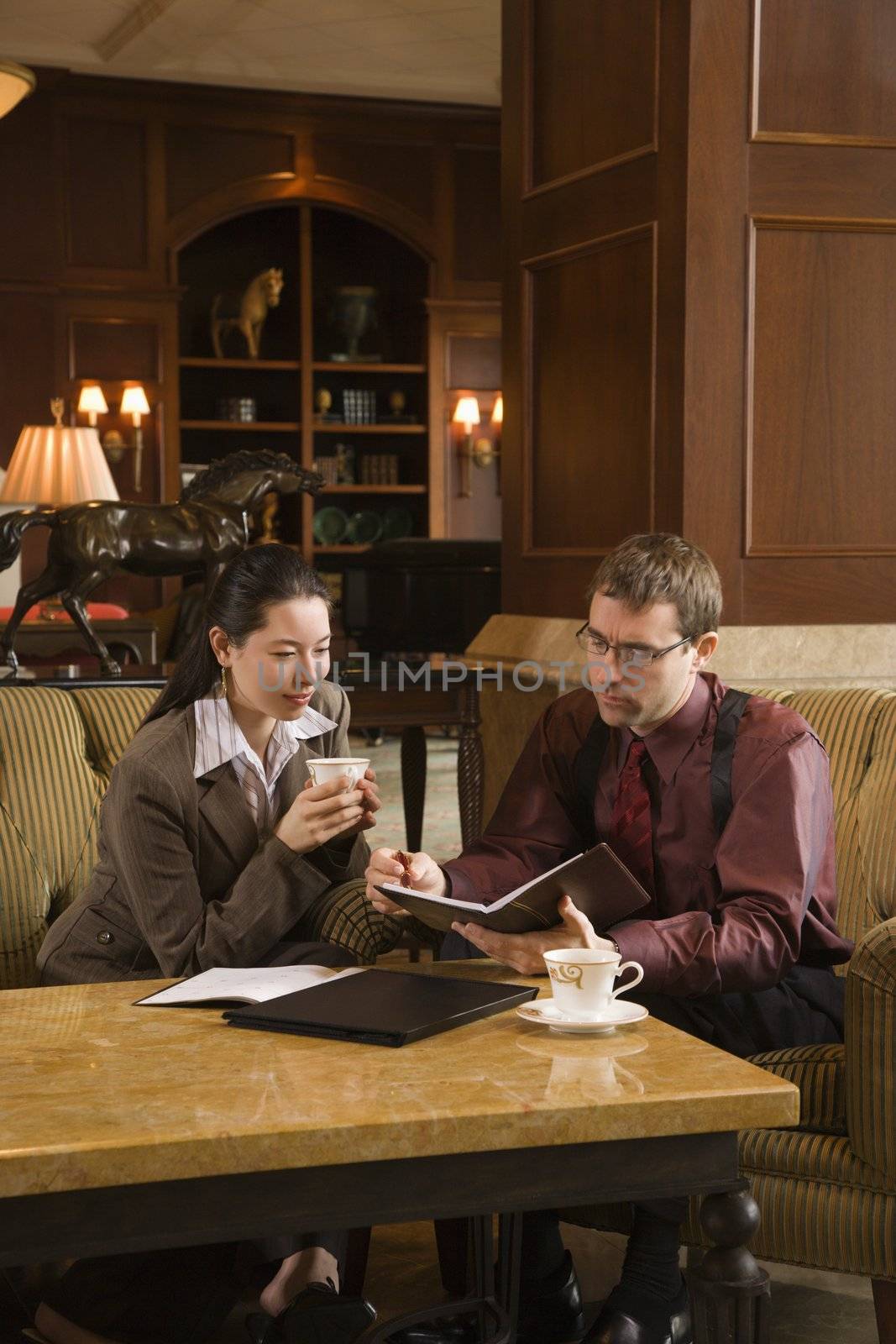 Caucasian mid adult businessman and woman drinking coffee and looking at portfolio.