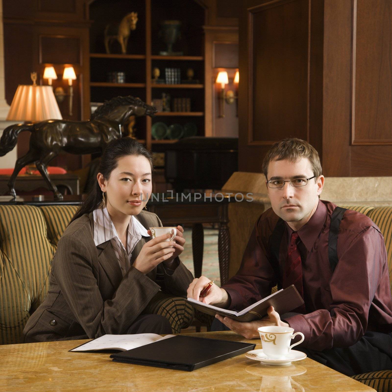 Caucasian mid adult businessman and woman drinking coffee and looking at viewer.