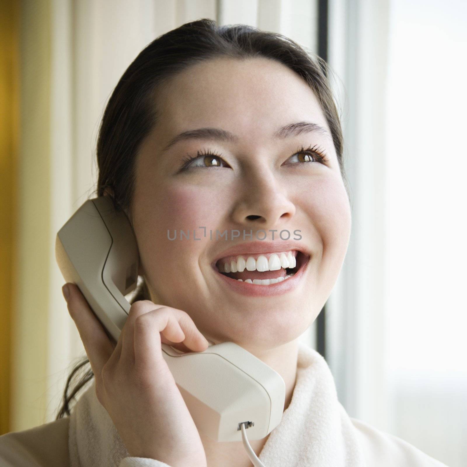 Taiwanese mid adult woman in bathrobe talking on phone and smiling.