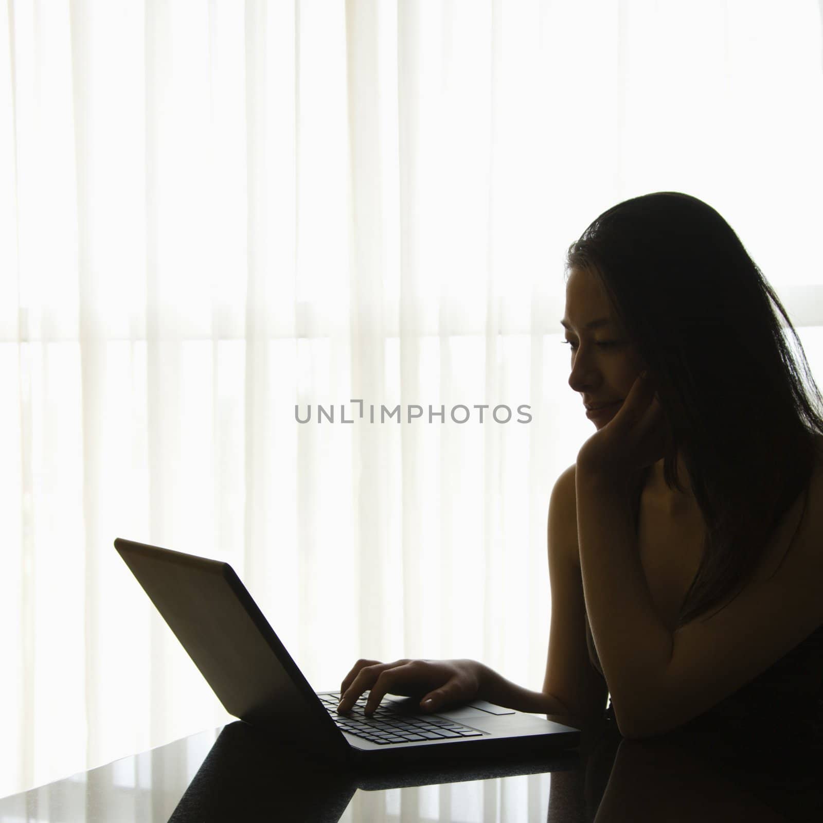 Silhouette of Taiwanese mid adult woman on laptop.