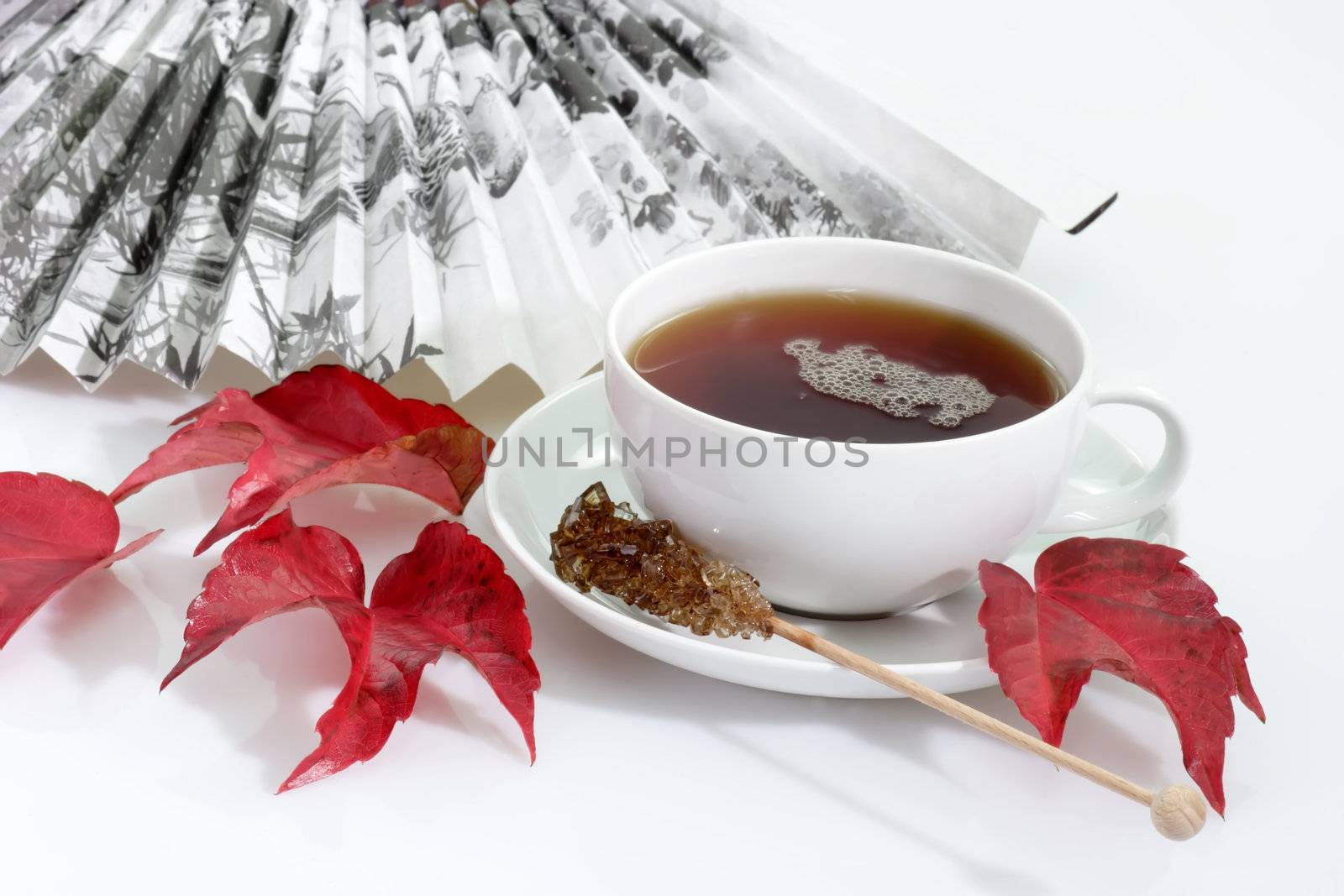 A cup of tea with fan and autumn foliage on bright background