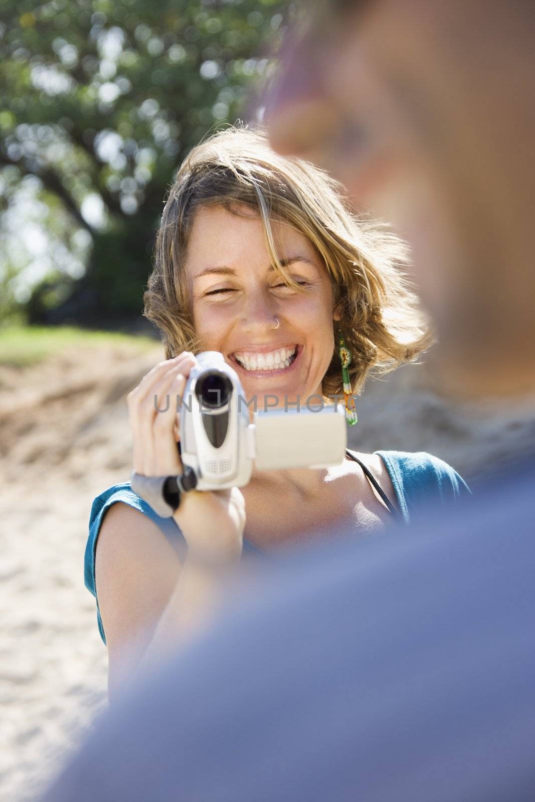 Mid-adult Caucasian woman outdoors pointing video camera at man.