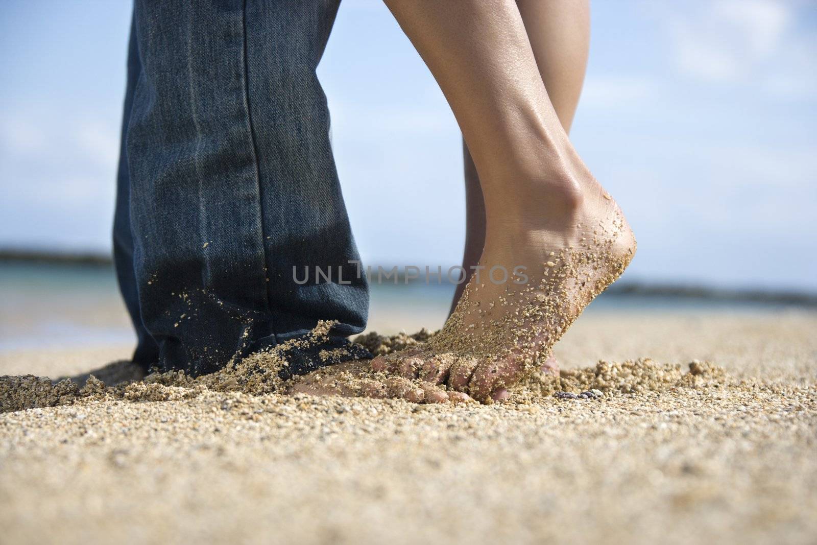 Feet and legs of mid-adult Caucasian couple standing together on beach.