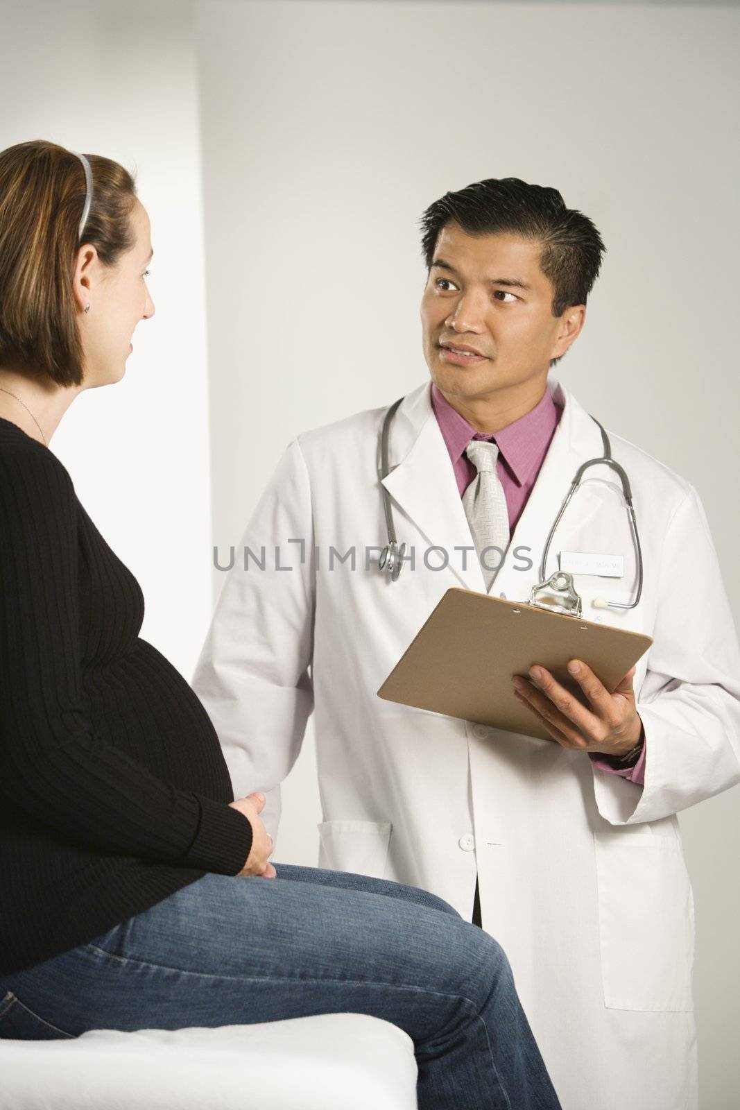 Asian American male doctor examining Caucasian pregnant female patient.