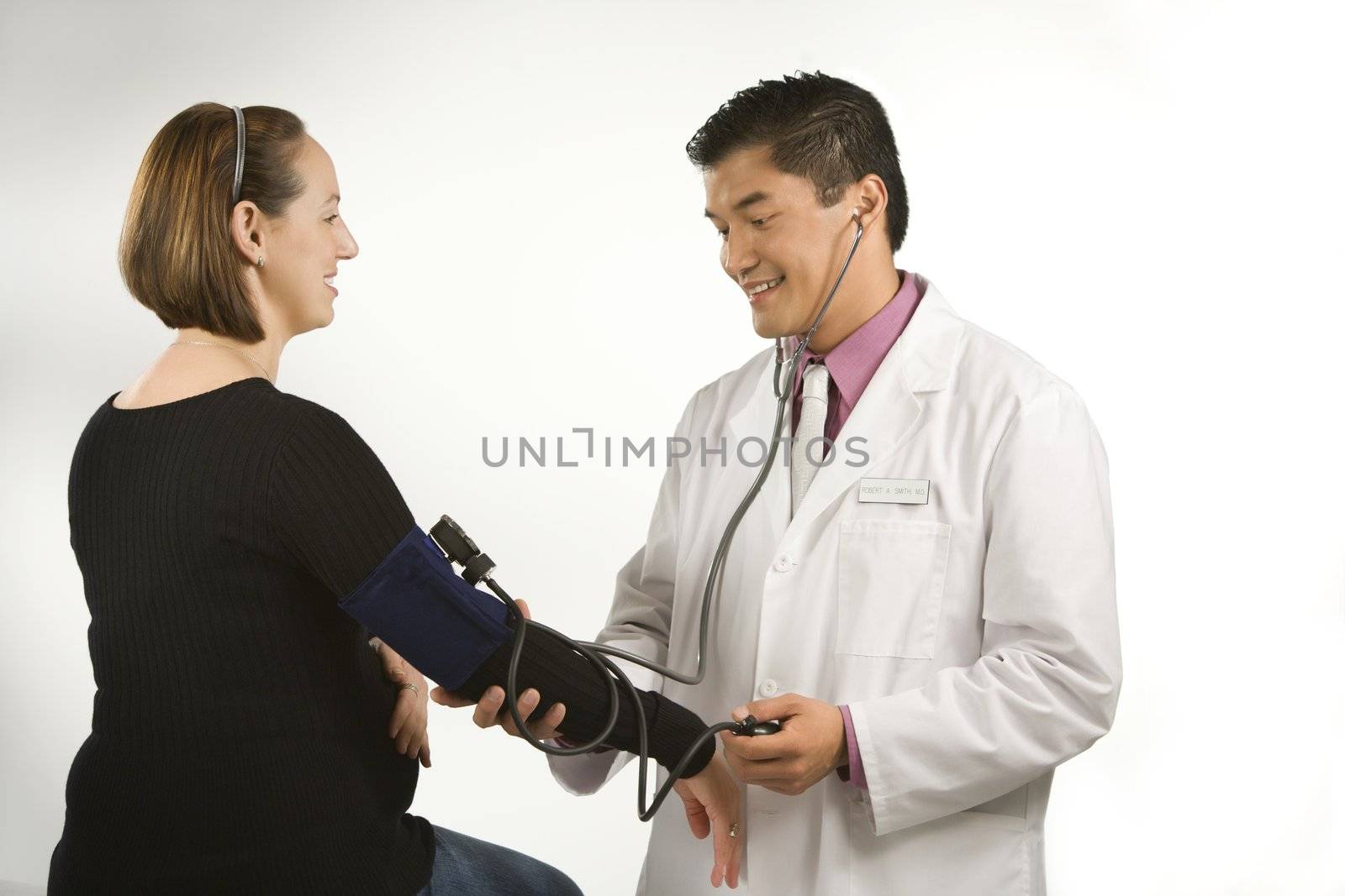 Asian American male doctor testing blood pressure of pregnant Caucasian woman.
